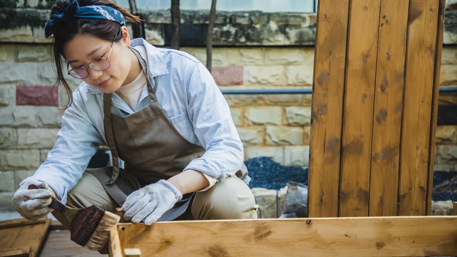 A woman applying wood sealant on a shelf