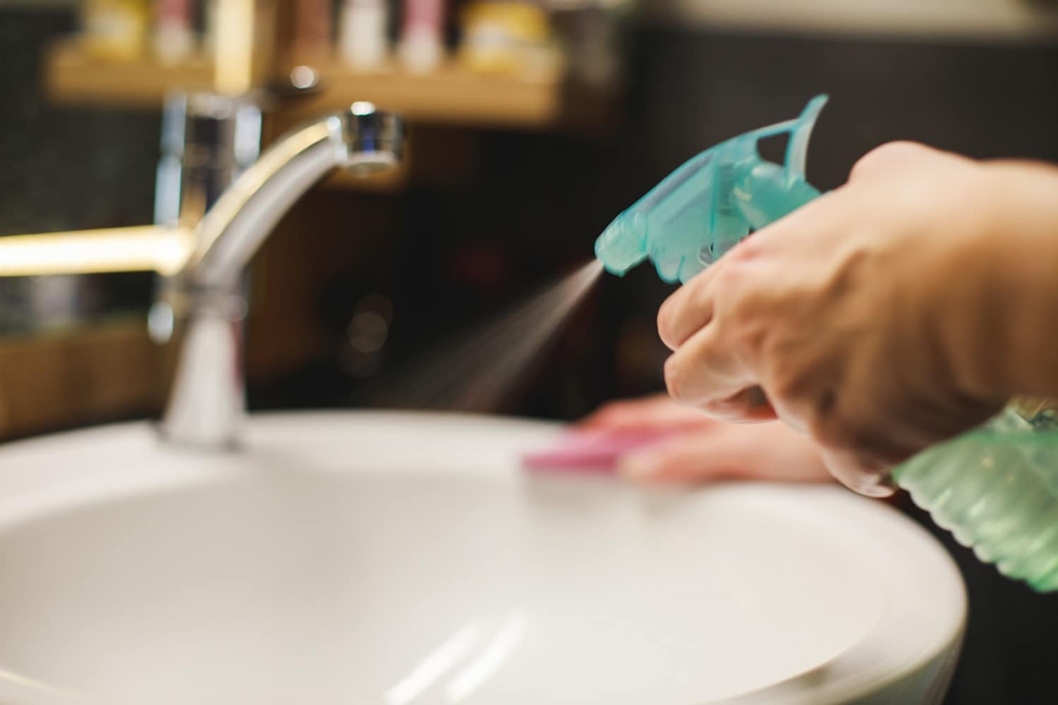 A woman using a spray to clean bathroom sink