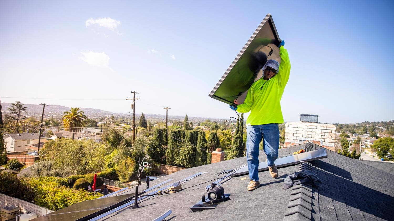 A worker installing a solar panel on the roof of a house