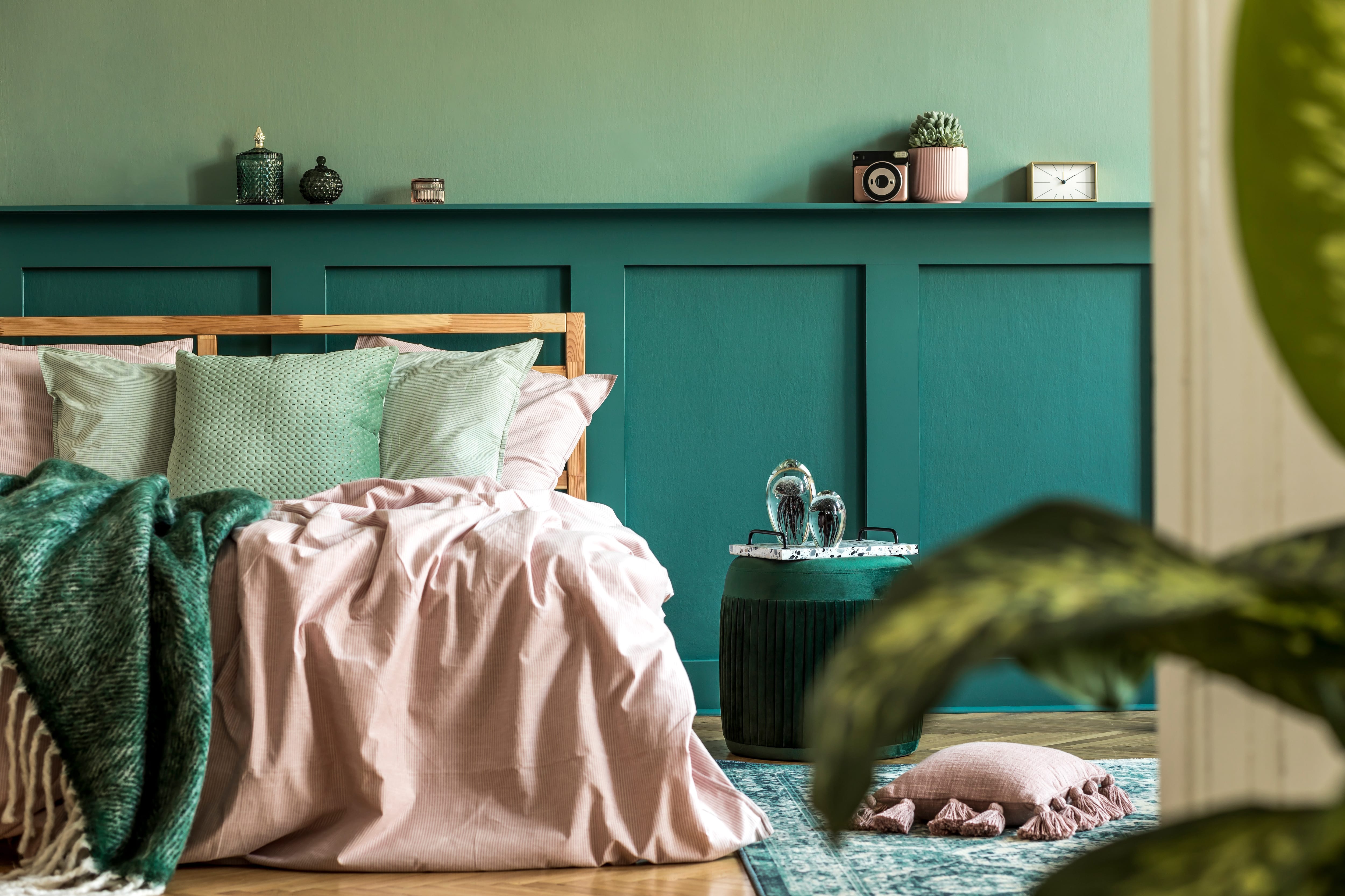 Bedroom with pink and green bedding, green rug, and emerald board and batten against moss green walls