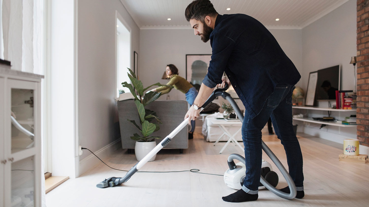 Man vacuuming floor while woman is cleaning the living room