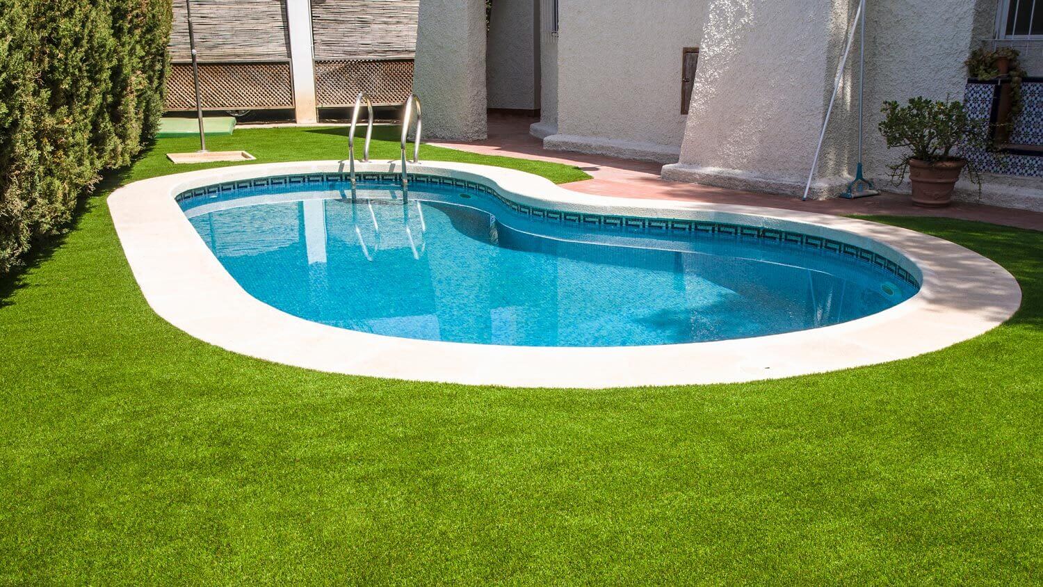 Artificial lawn around a swimming pool in a house’s backyard