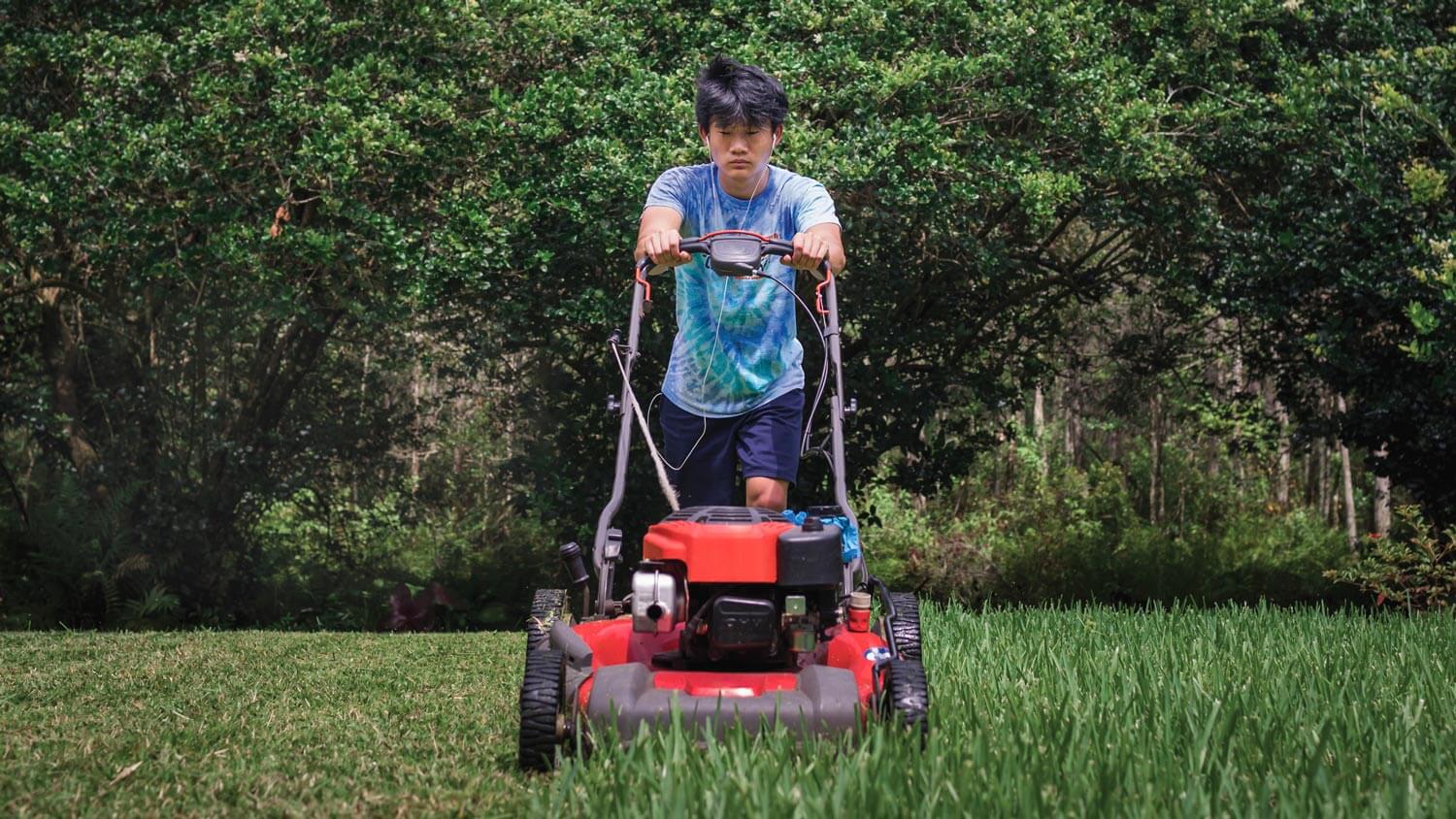 A teen boy mowing the grass in the garden