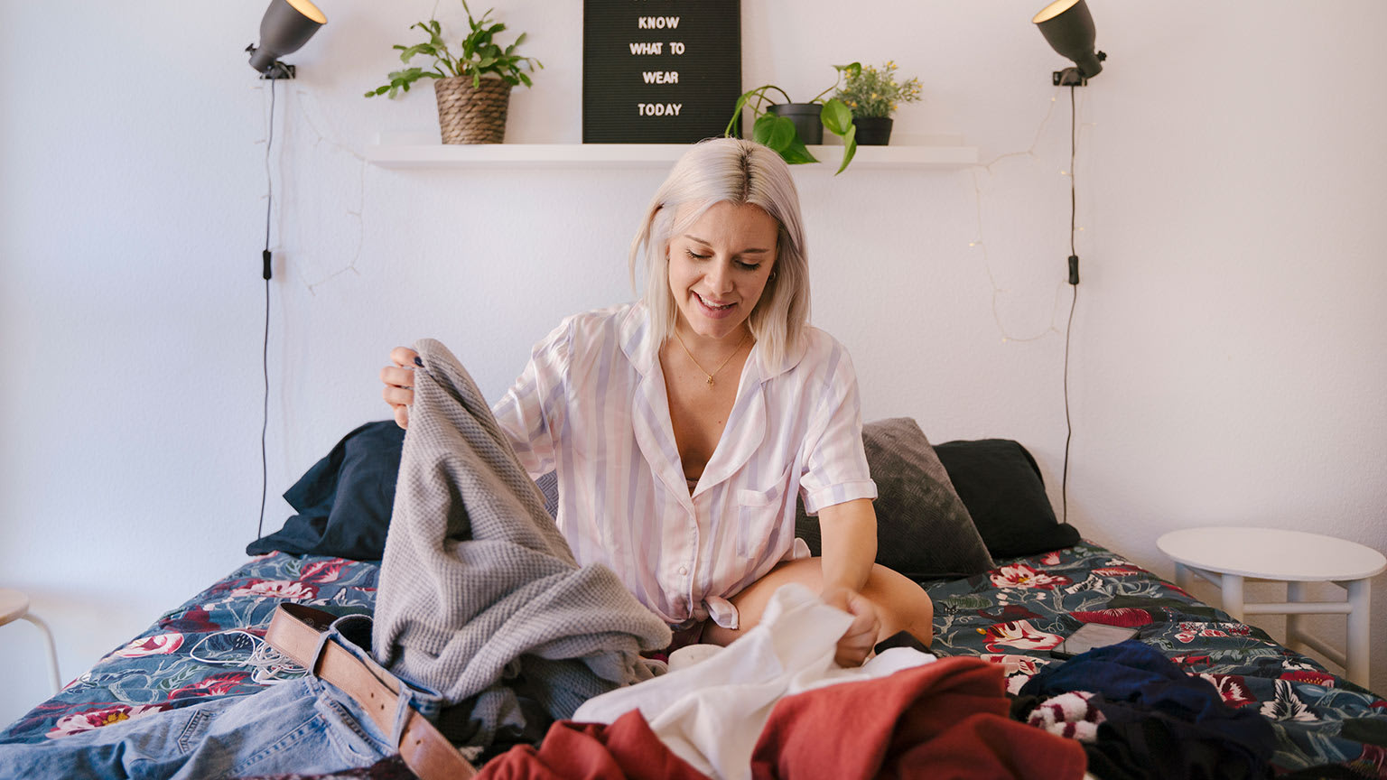 blonde woman choosing clothes on a bed