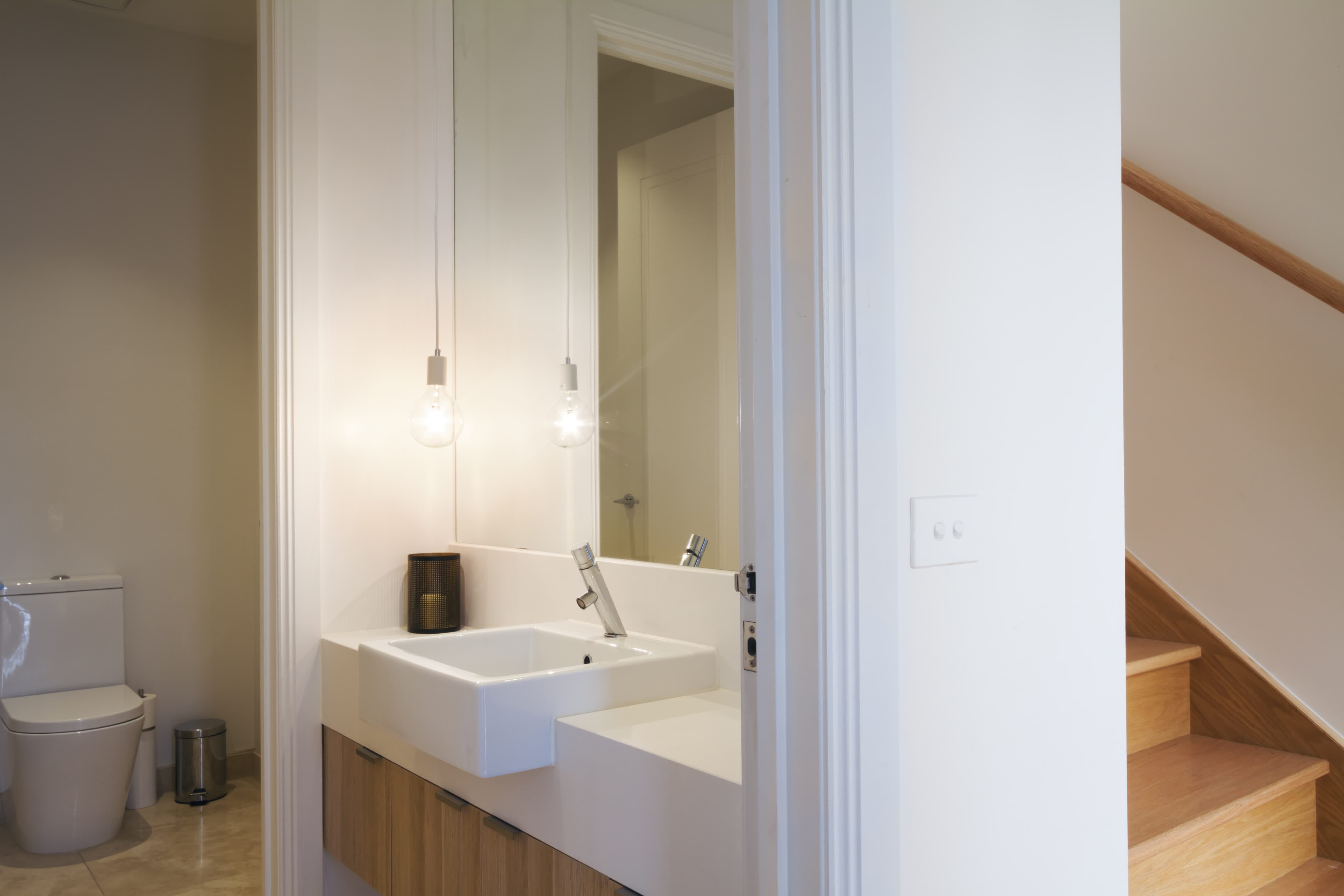 Modern minimalist bathroom with wooden countertop, two sinks, and black metal pendant lights