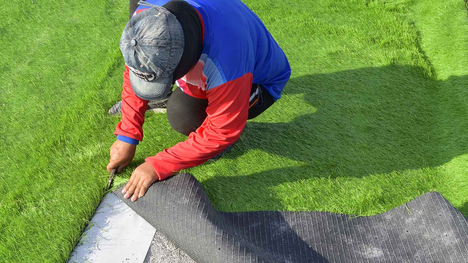 Gardener using utility knife to cut artificial grass edges