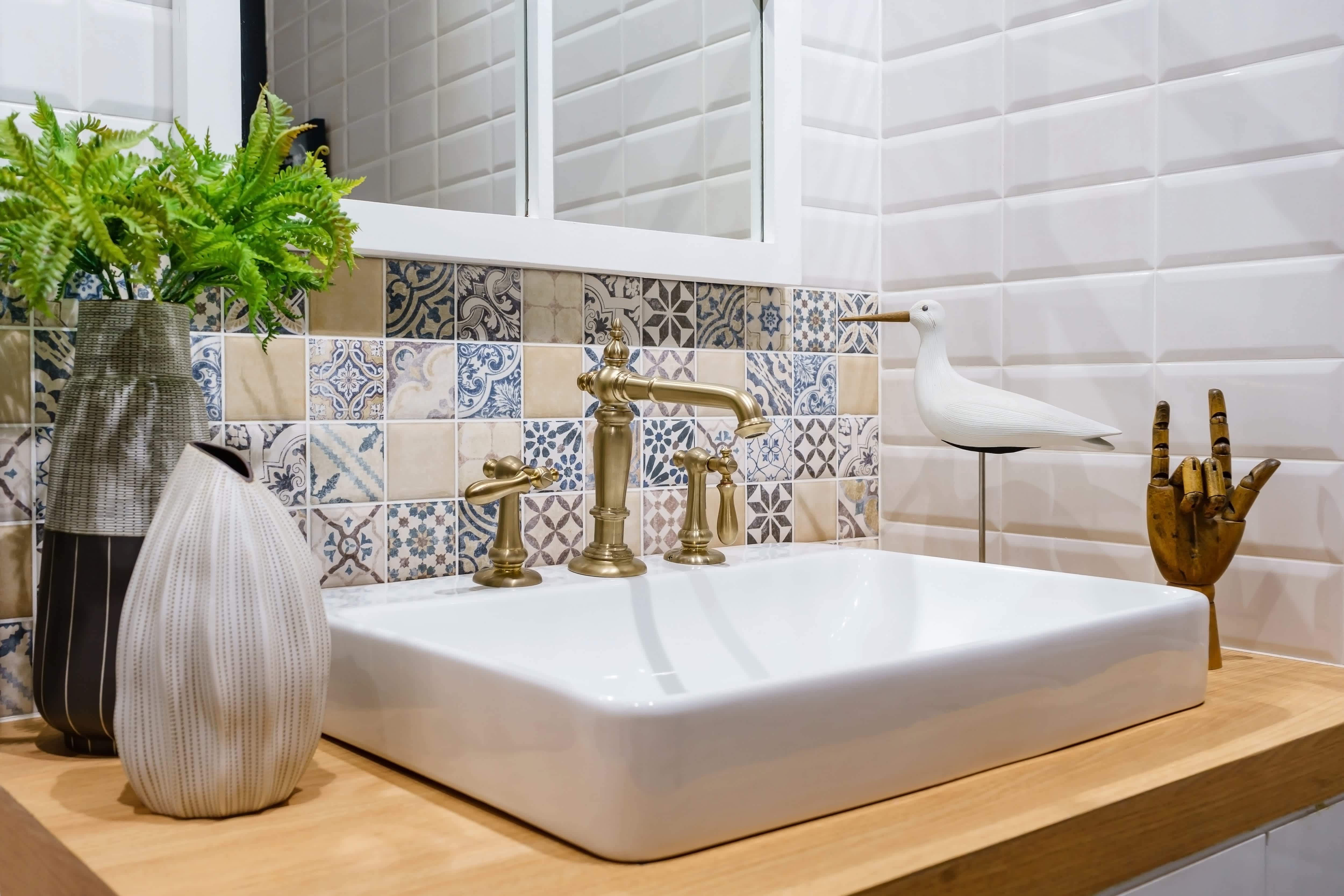 Modern bohemian style bathroom with geometric tiles, sculpted vases, gold fixtures, and wooden decorative accents
