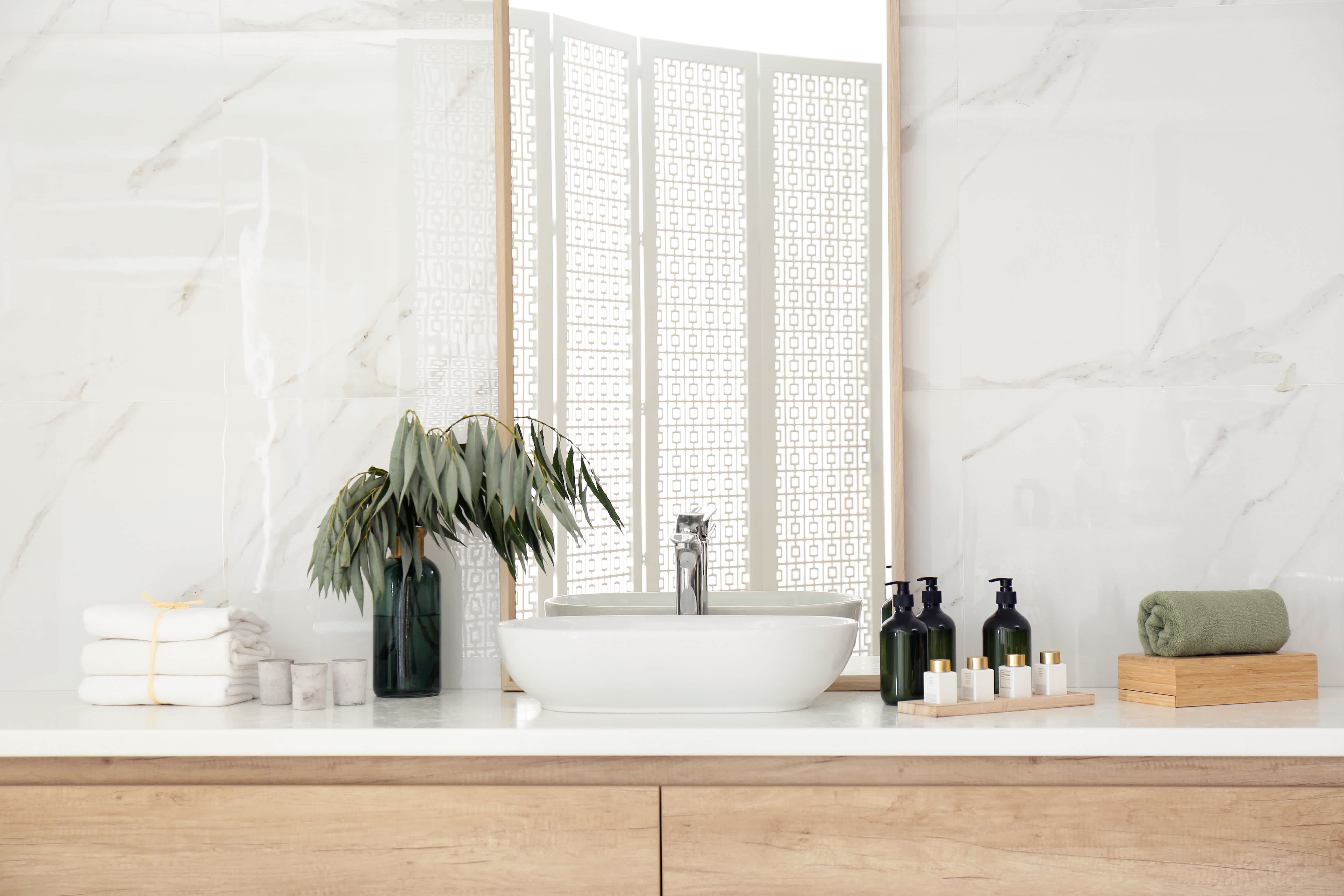 Minimalist bathroom with white countertop, white walls, light wood vanities, and countertop sink