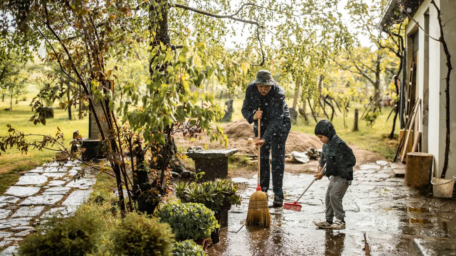 A father and son sweeping water from front yard on rainy day
