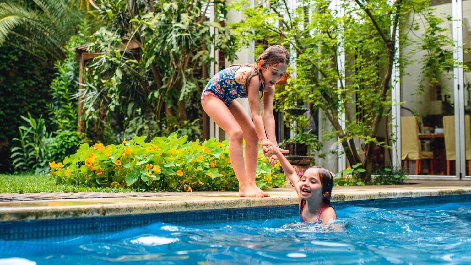 Sisters having fun at the backyard pool surrounded by a lush garden