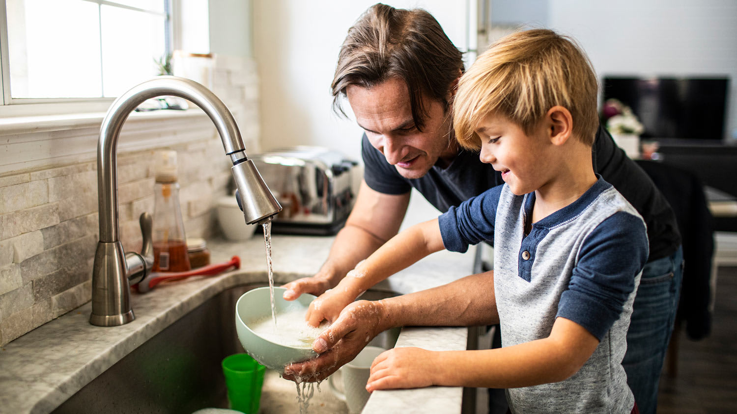 Father and son wash dishes in the kitchen sink