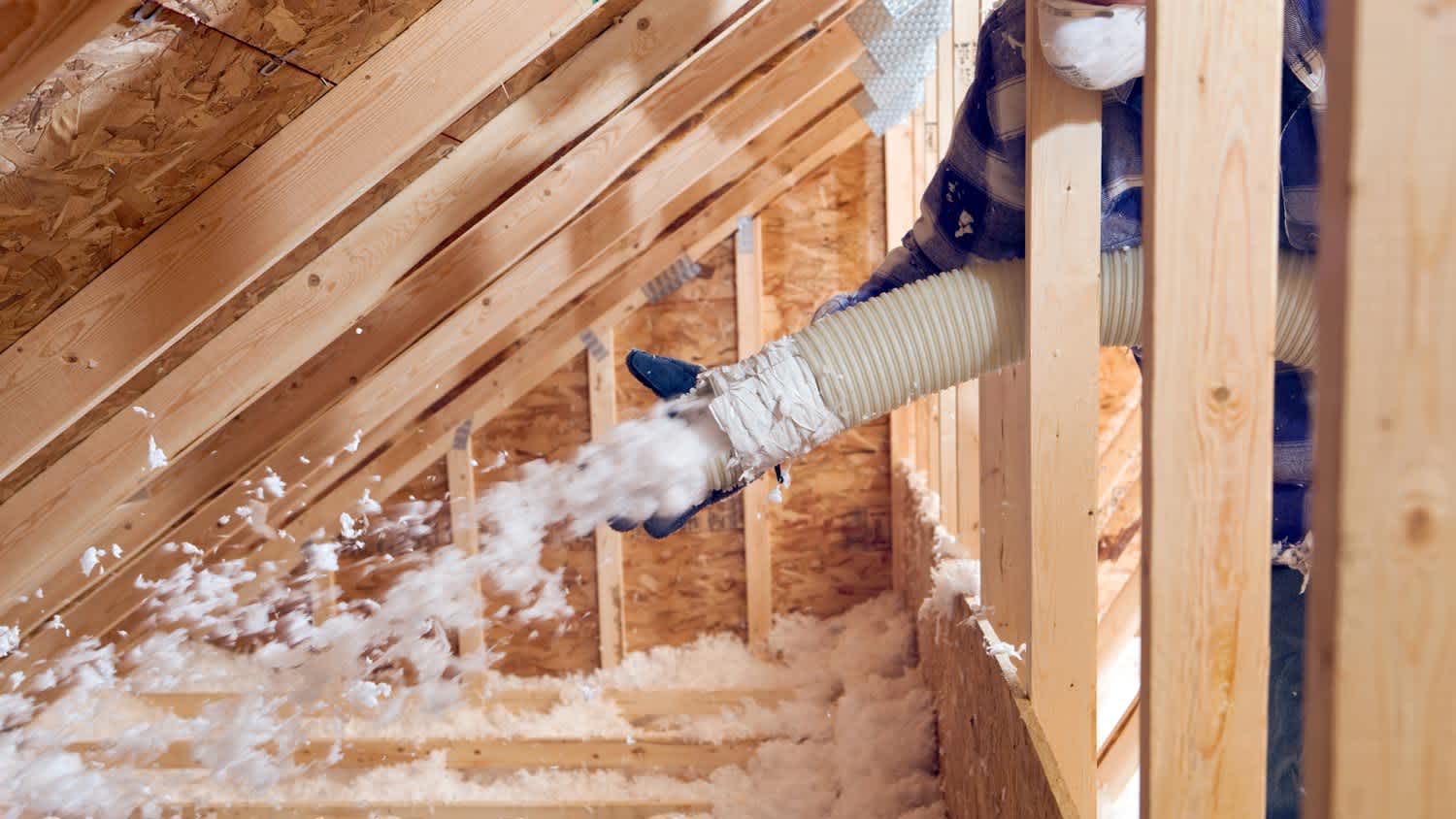 A worker using a blown-in insulation machine to insulate an attic