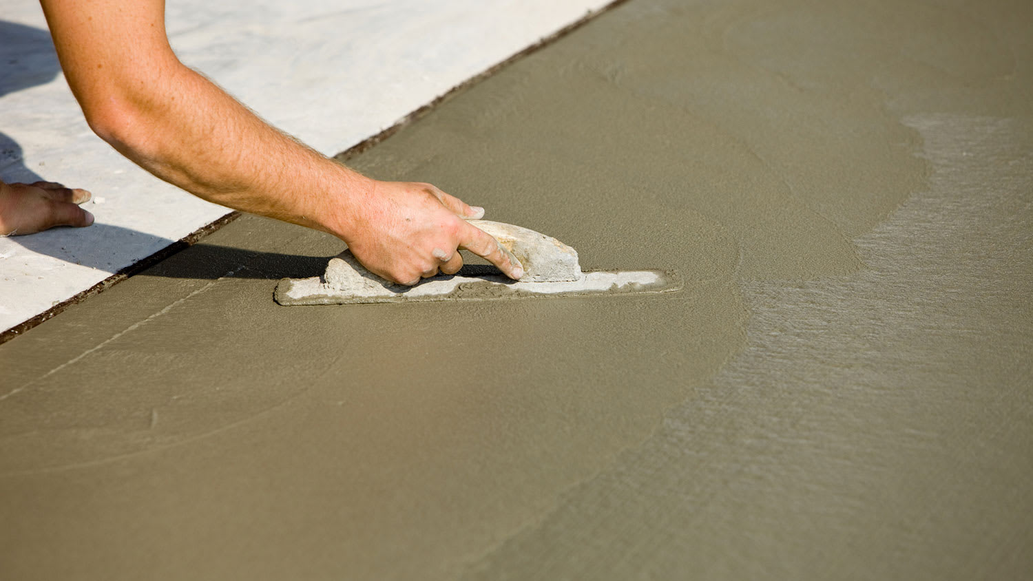 Worker using concrete trowel to smooth fresh concrete