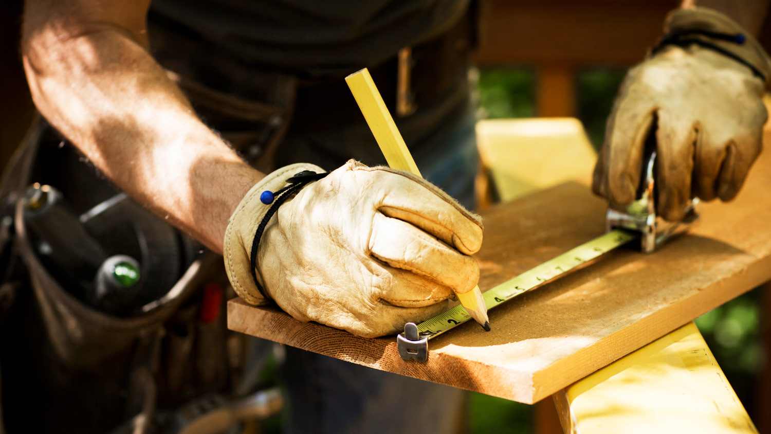Close-up of a carpenter’s hands in gloves measuring a wooden plank