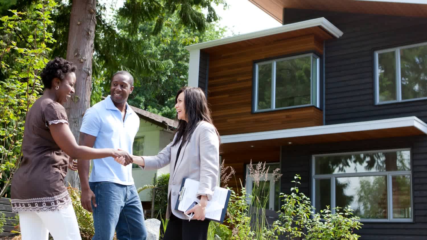 A real estate agent greeting couple at house