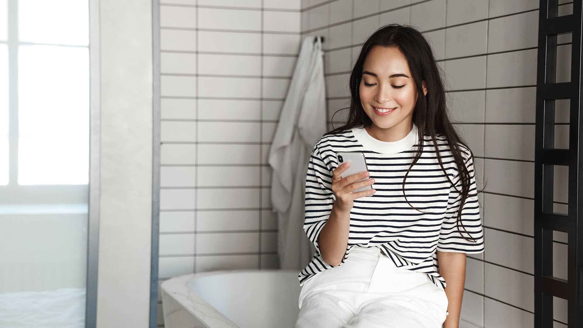 woman sitting on bathtub looking at her phone