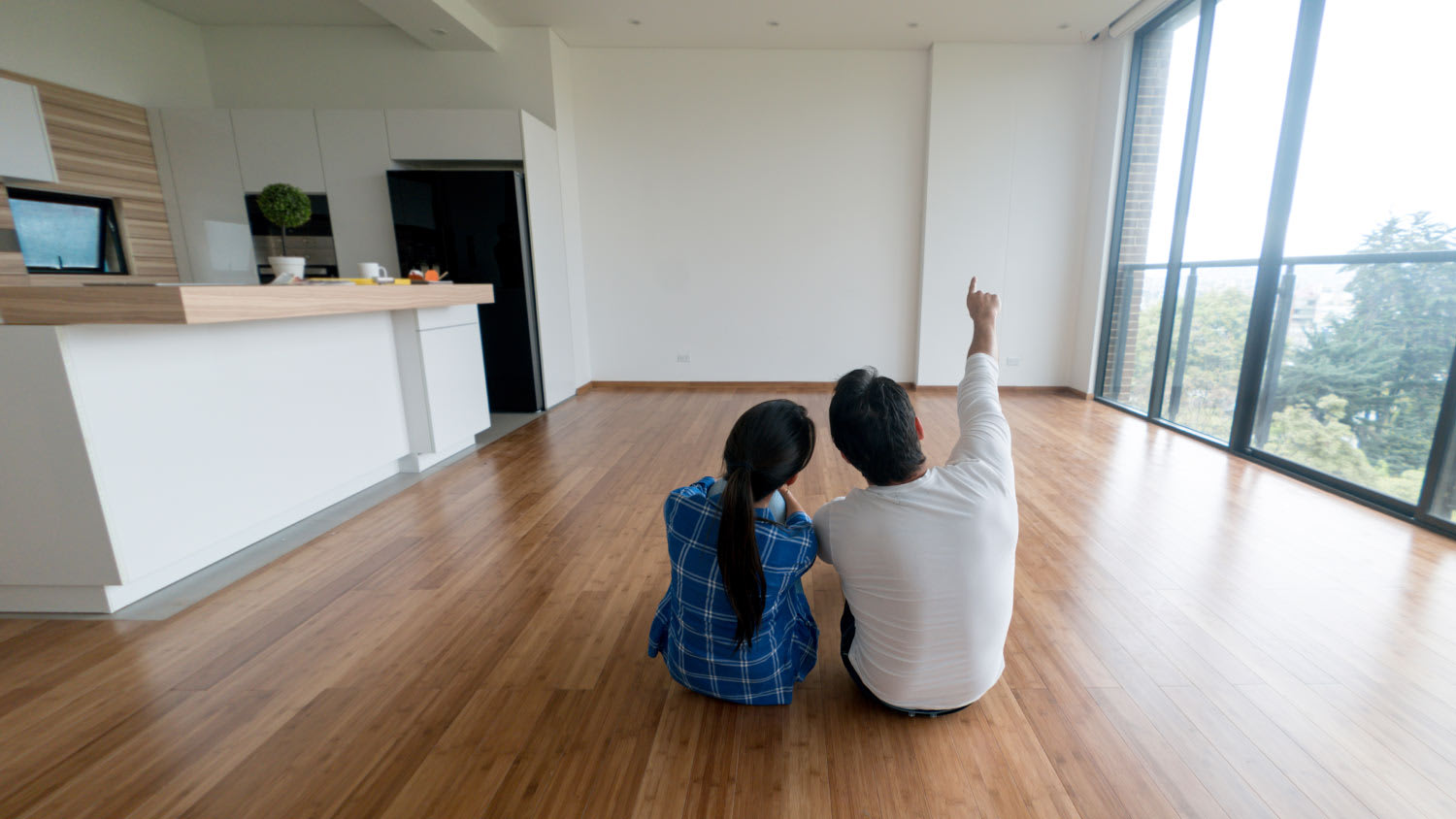 couple sitting on hardwood floors looking at new apartment
