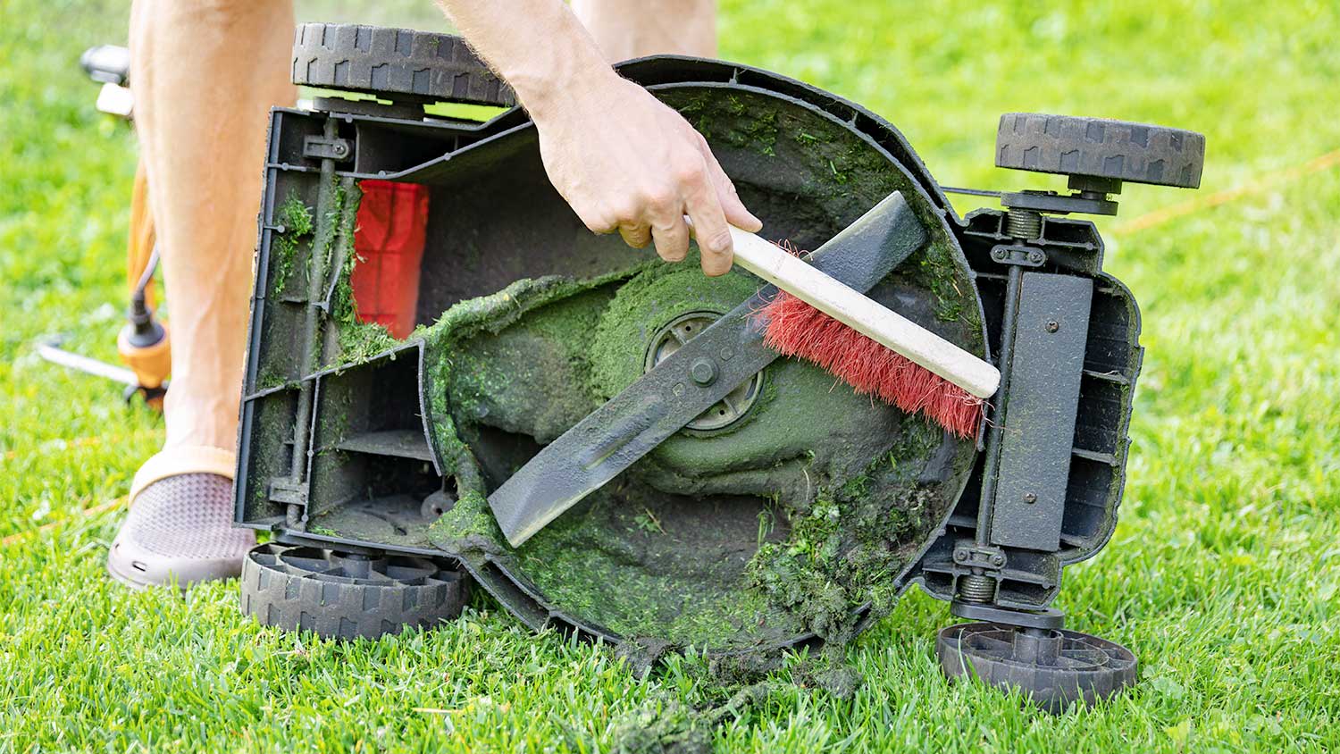 A man cleans the underside of a lawn mower