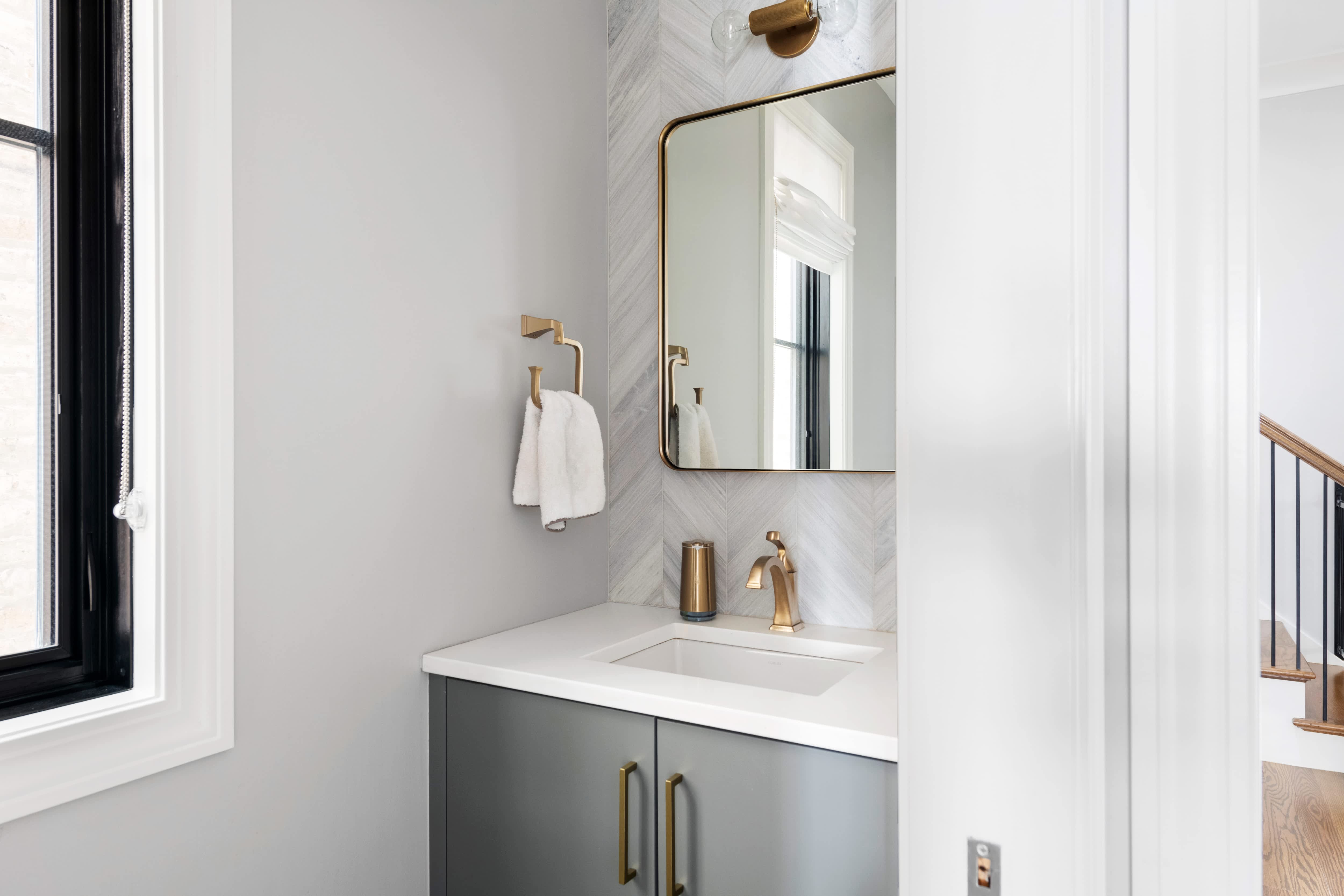 Contemporary powder room with gray vanity, white countertop, and chic bronze mirror