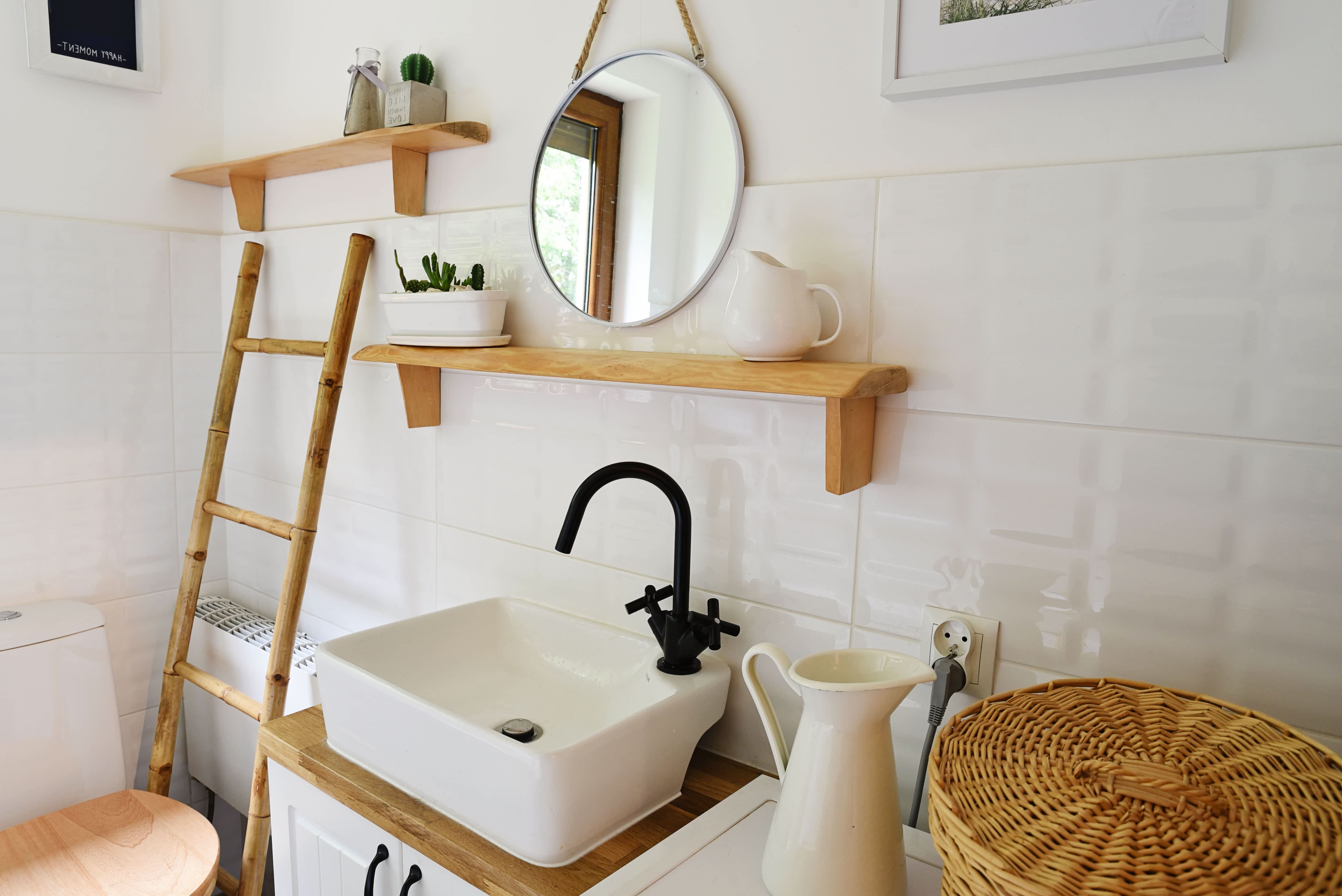 Small farmhouse-style bathroom with exposed shelving, round mirror, white sink, and wooden accent