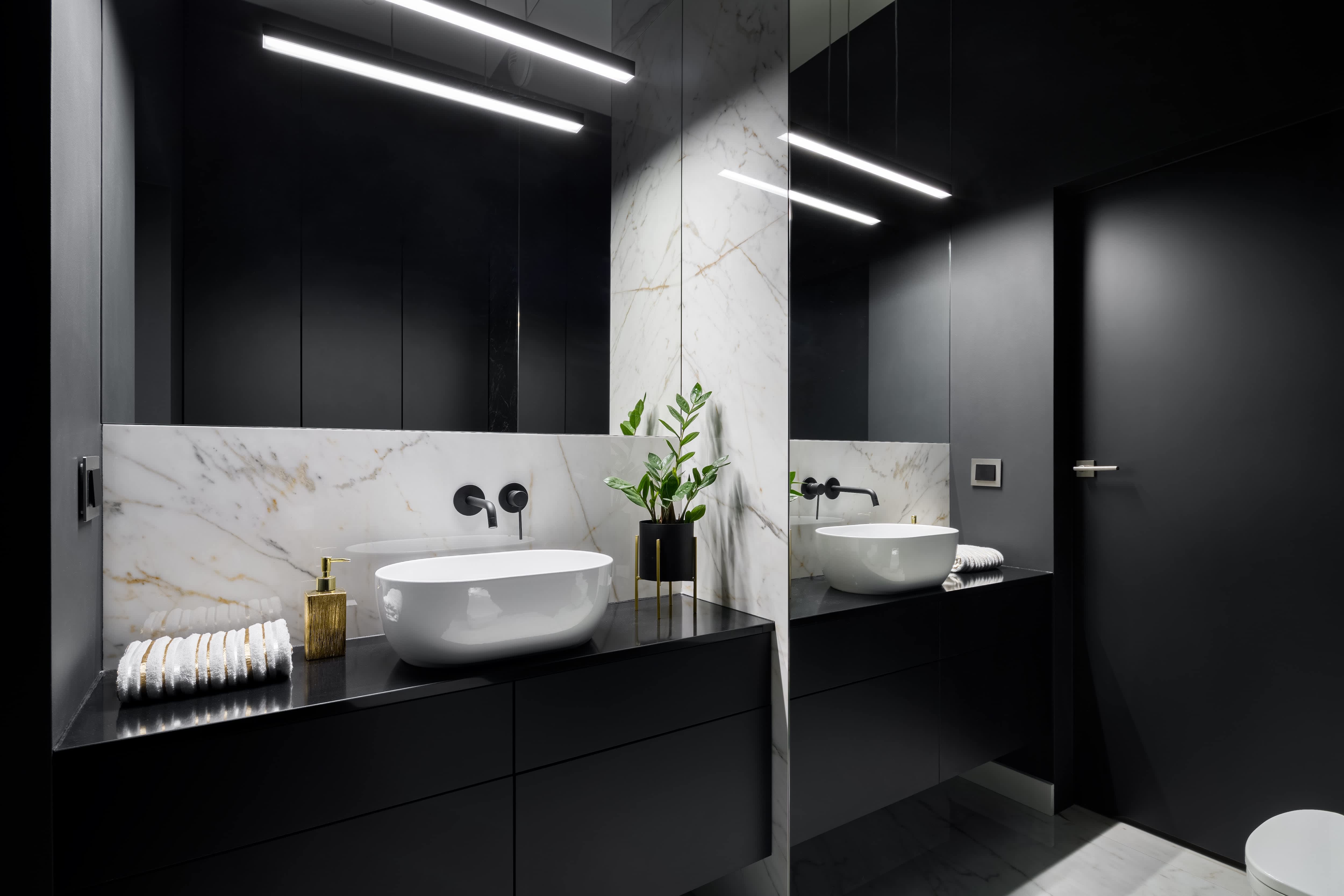Small powder room with black walls, white marble accents, a white vessel sink, and full-length mirror