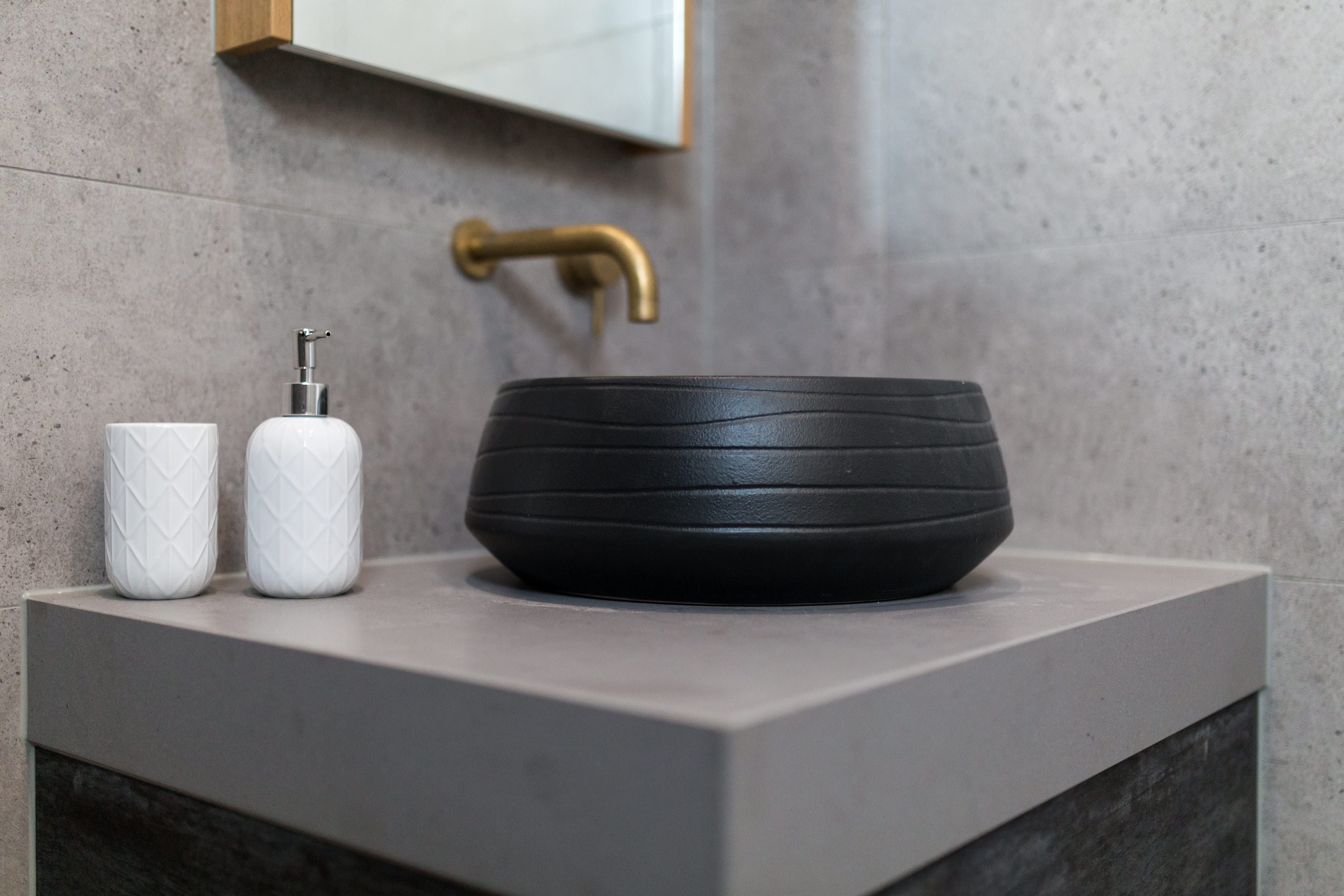 Modern bathroom with gray marble tile, black sink, and gold hardware