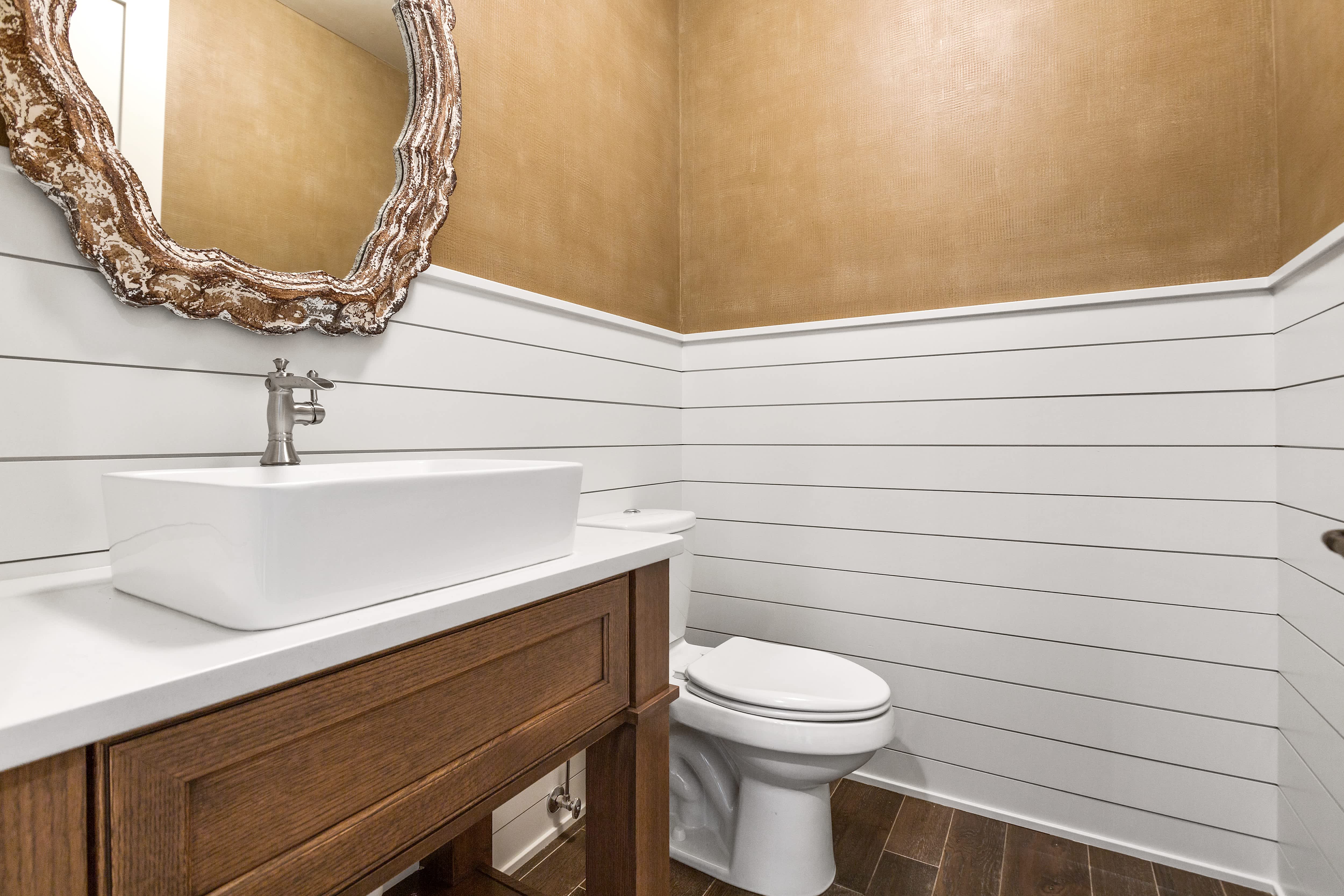 Modern powder room with vessel sink, wooden cabinet, white toilet, gold walls, and shiplap paneling