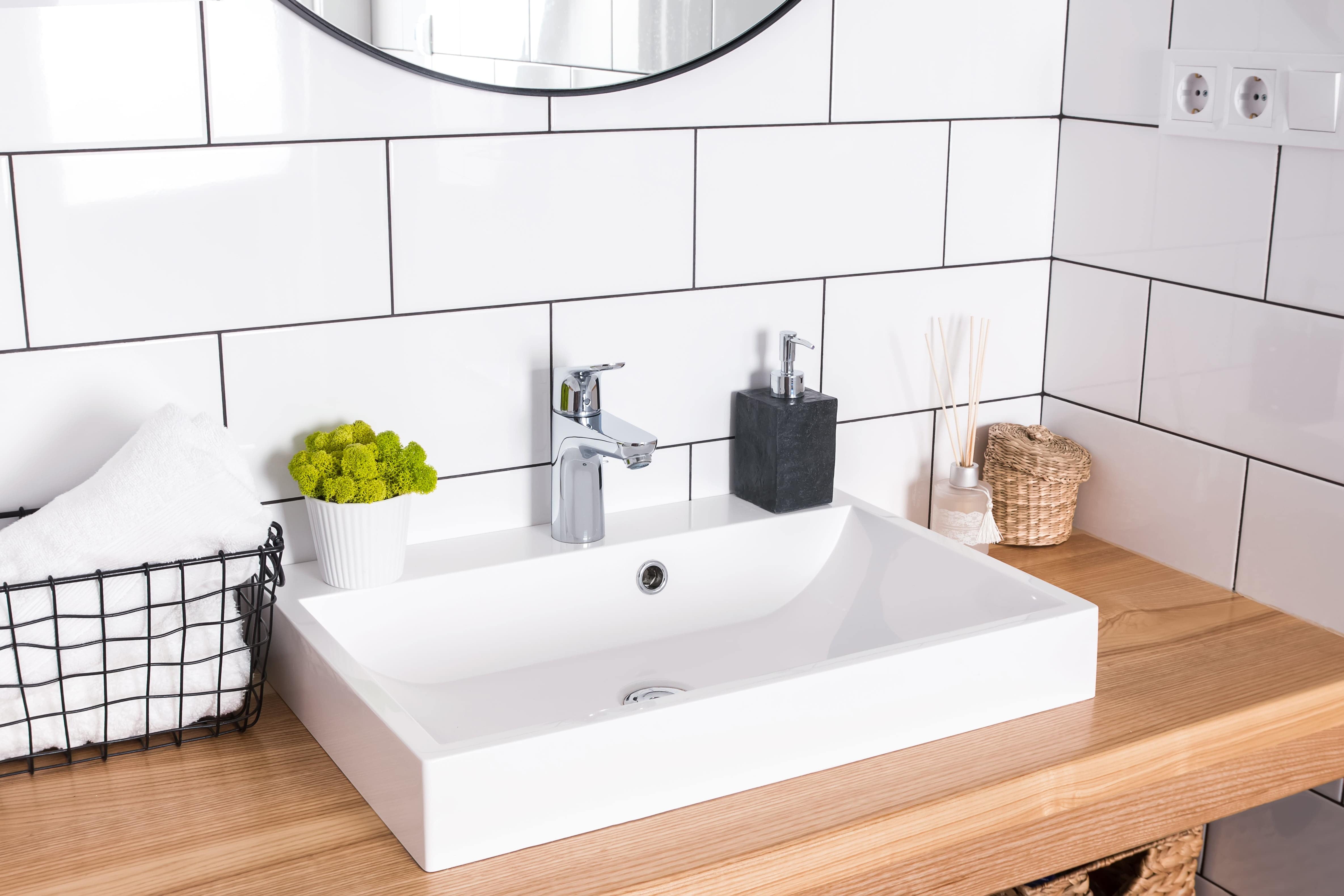 Bright, modern powder room with wooden vanity, white sink, and white subway tile