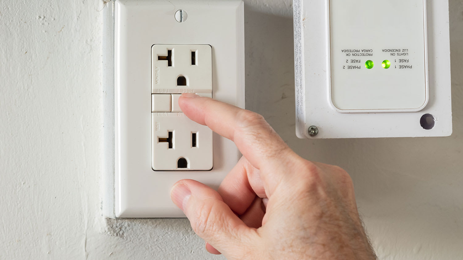 Hand pressing reset button on a GFCI outlet