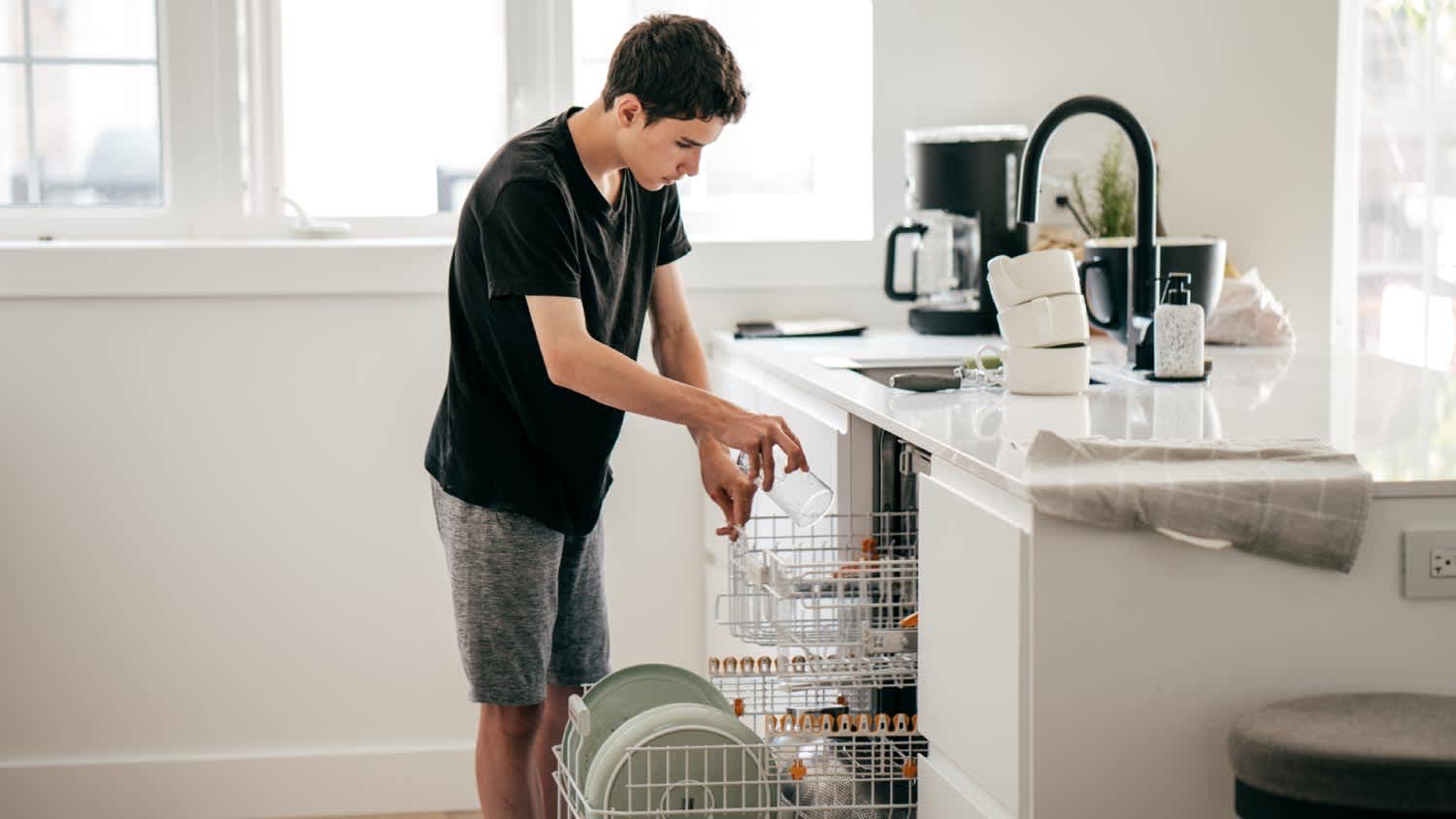 A teeneger putting dishes in dishwasher machine