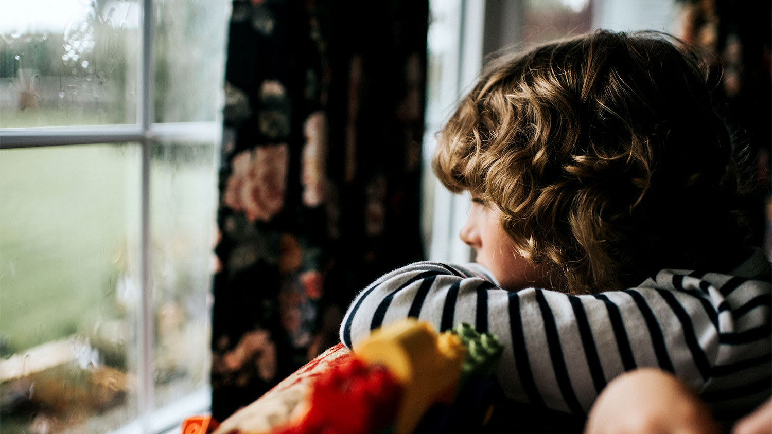 A child looks out a window at a storm