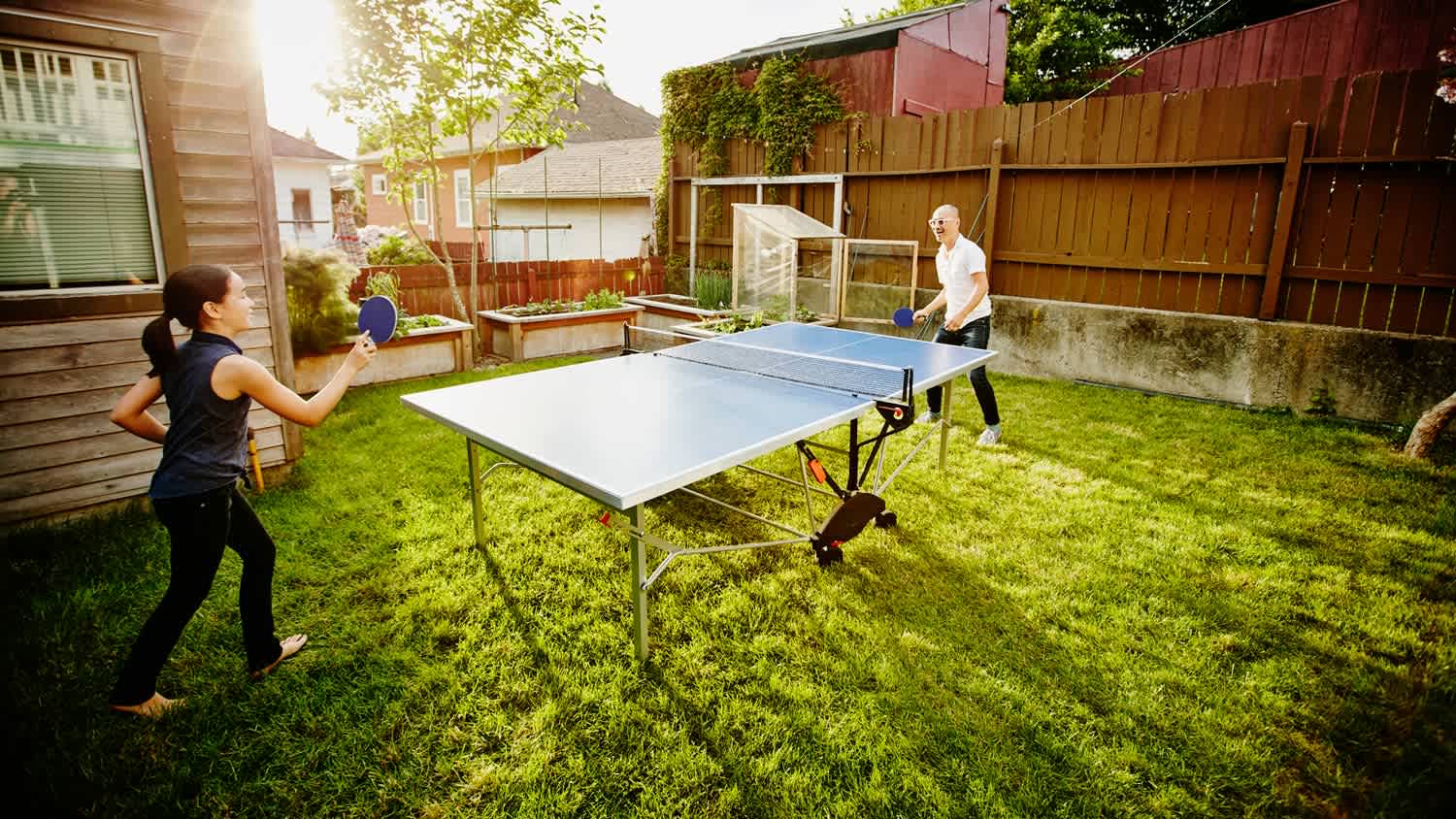 A daughter and her father playing ping pong in their backyard