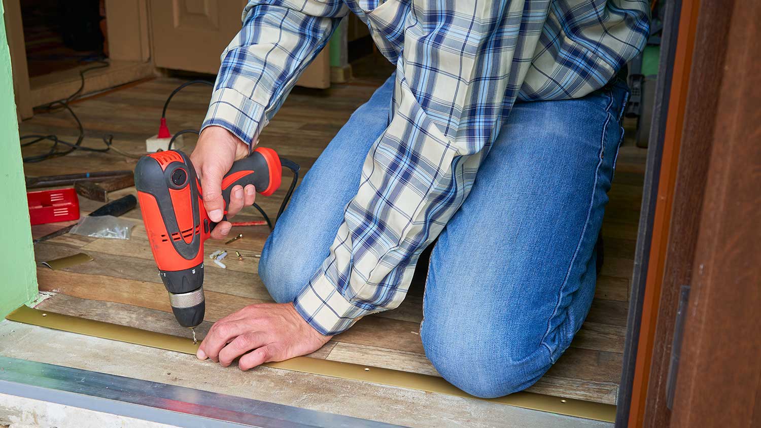 Worker drilling the floor to install doorway floor strip