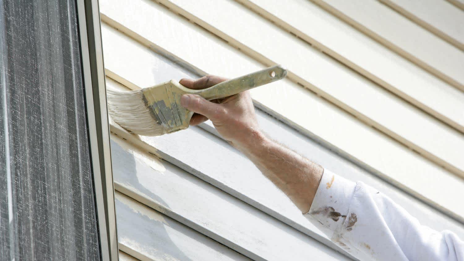 A man painting the vinyl siding of a house