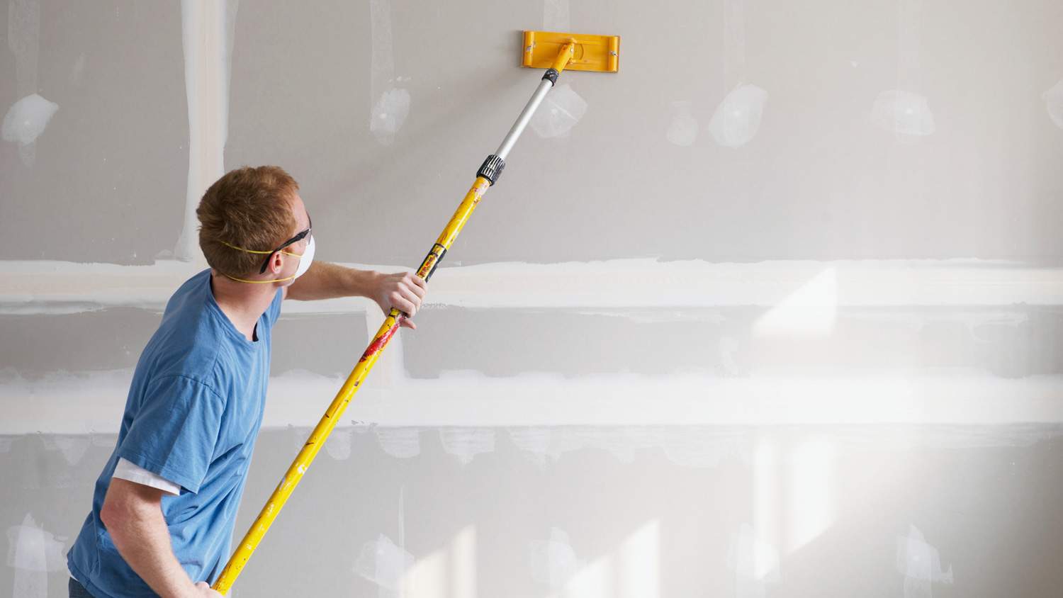 A young man sanding a drywall
