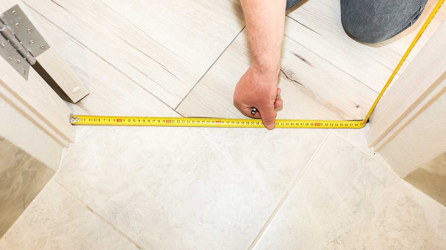 Worker using measuring tape to install doorway transition strip