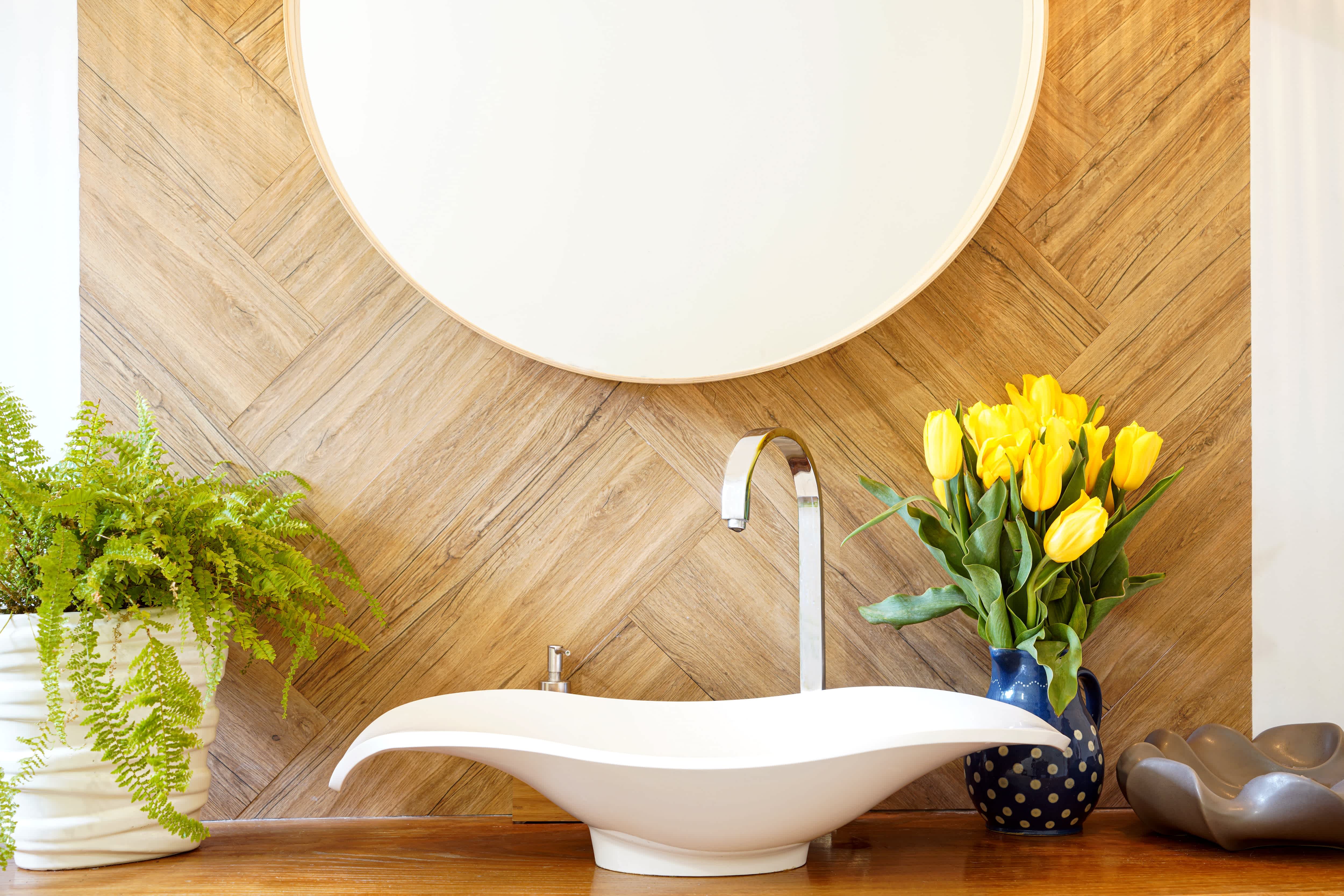 Bohemian style bathroom featuring floating vanities, wood paneling, a round mirror, white modern sink, and fresh flowers