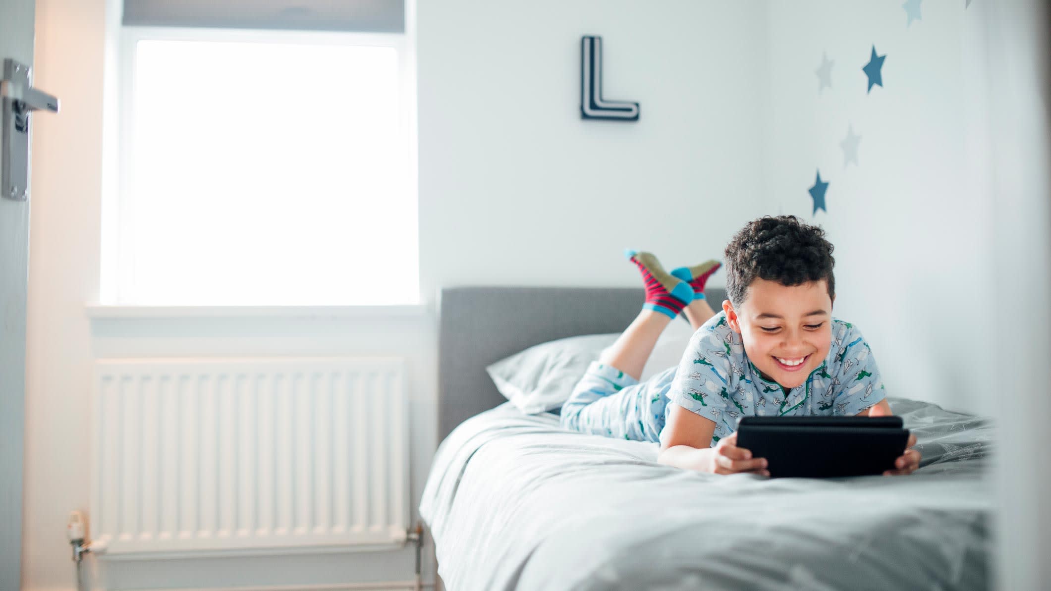 A boy playing games on a digital tablet on his bed