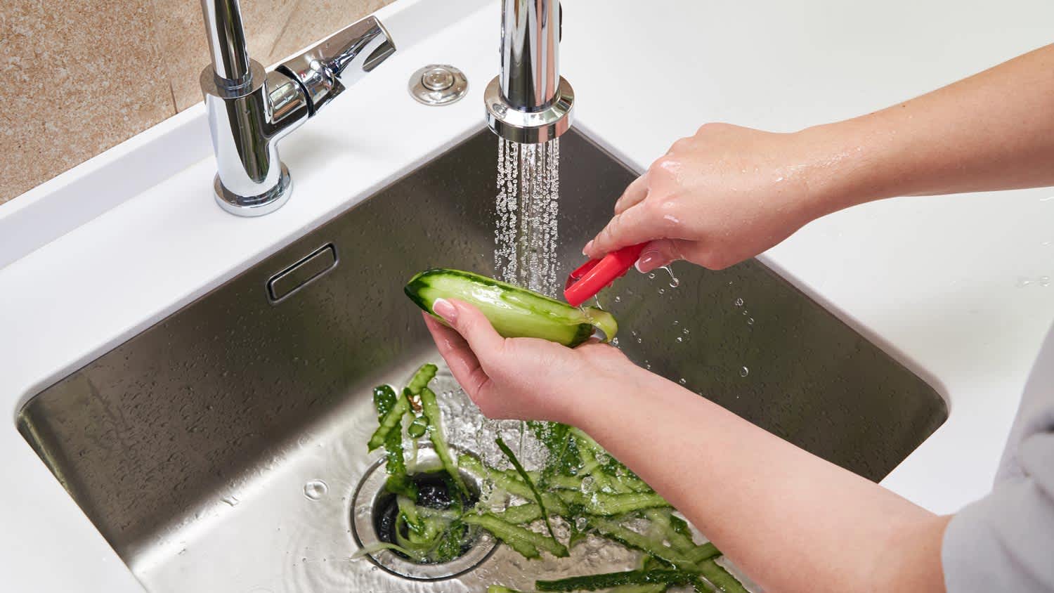 A woman peeling a cucumber over a garbage disposal
