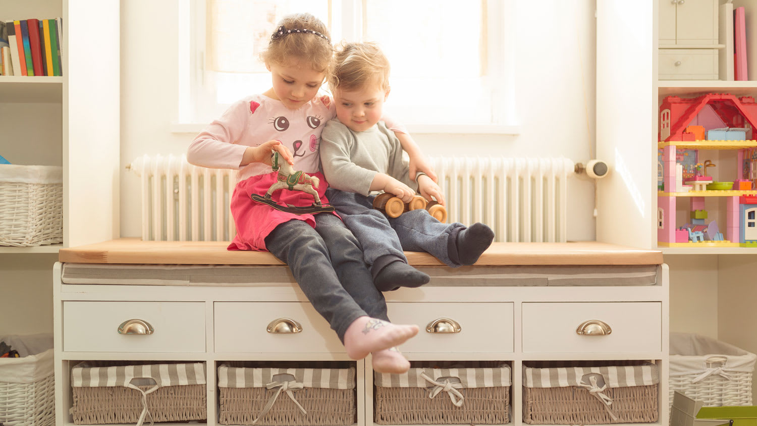Siblings sitting on window seat and playing with toys