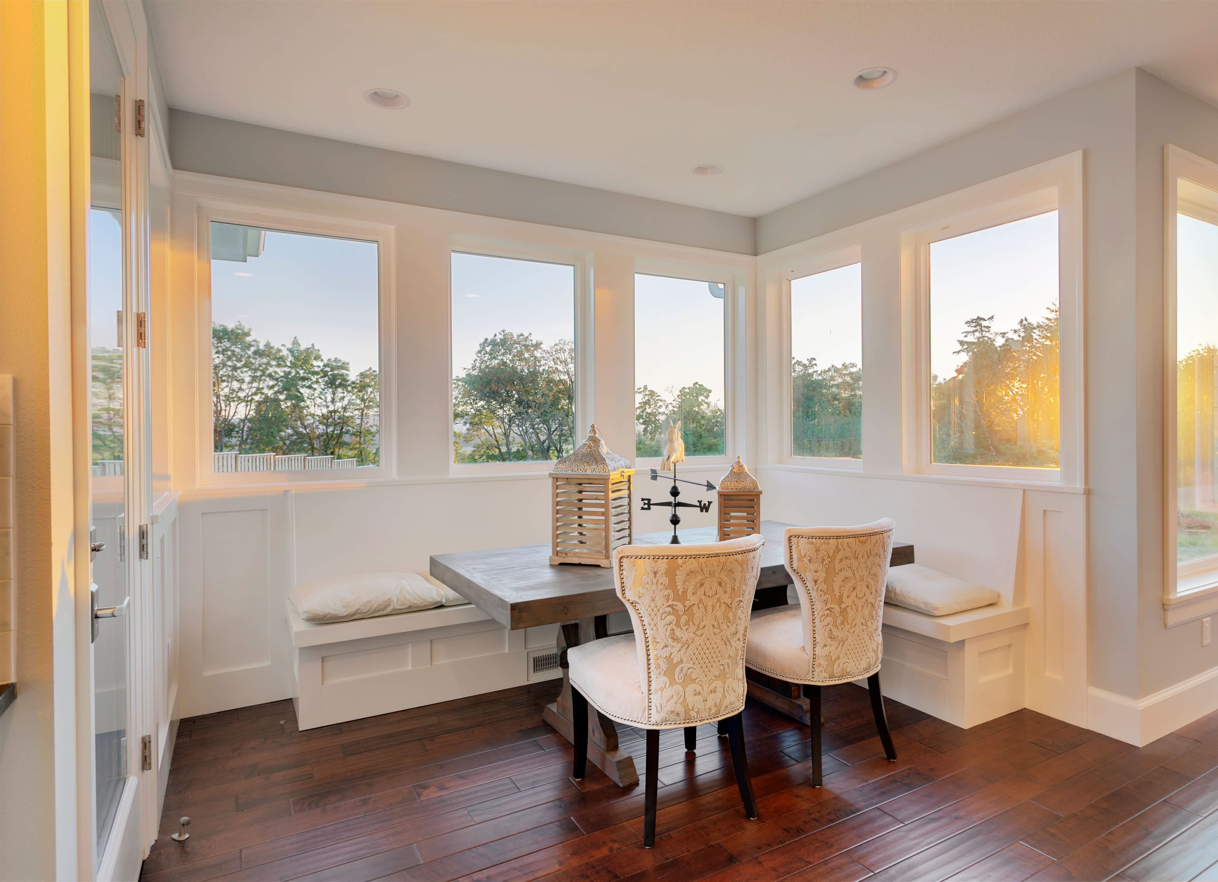 A spacious breakfast nook area with white bench seating next to a wall of windows