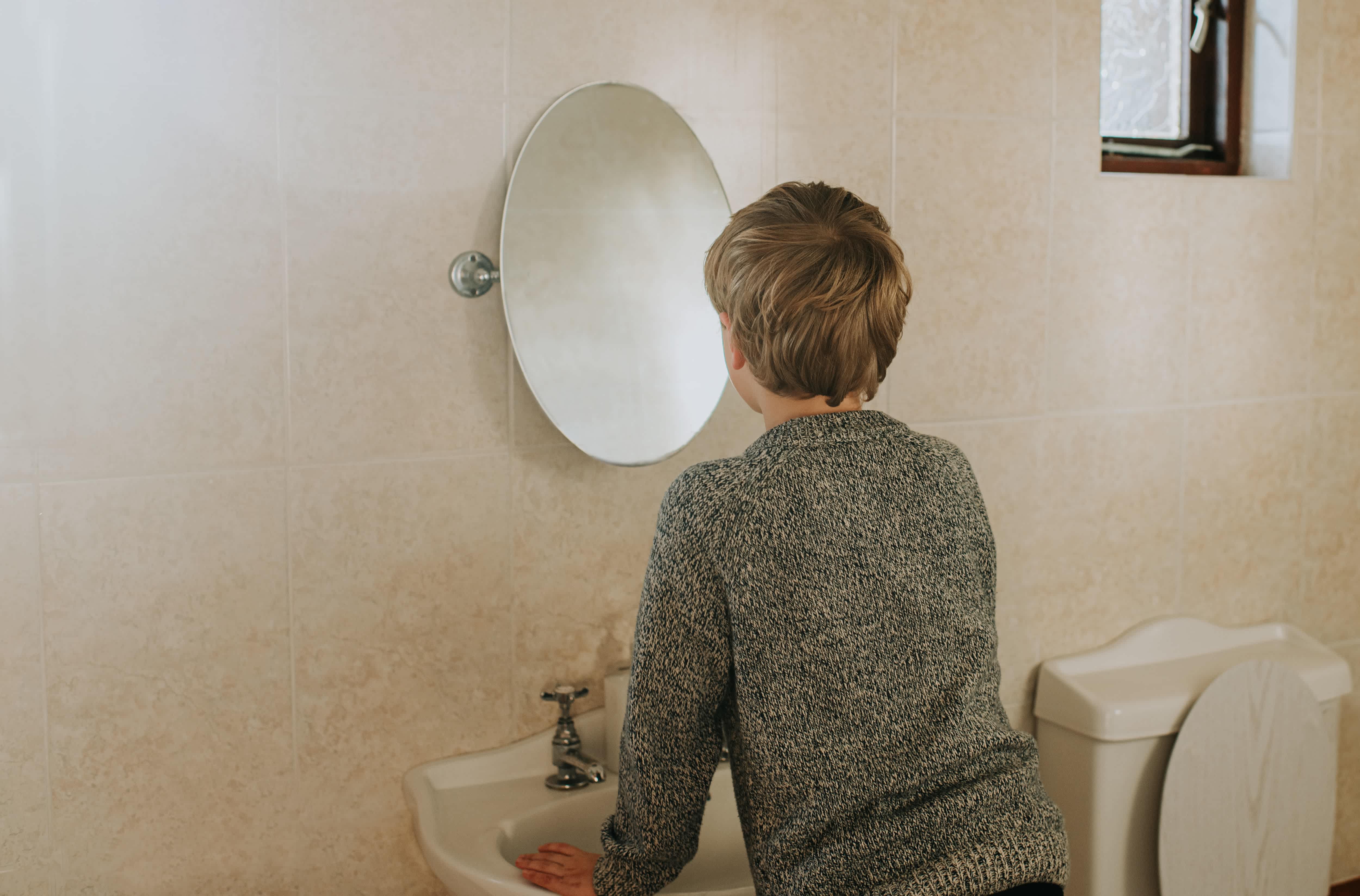 Boy standing in front of oval pivot mirror