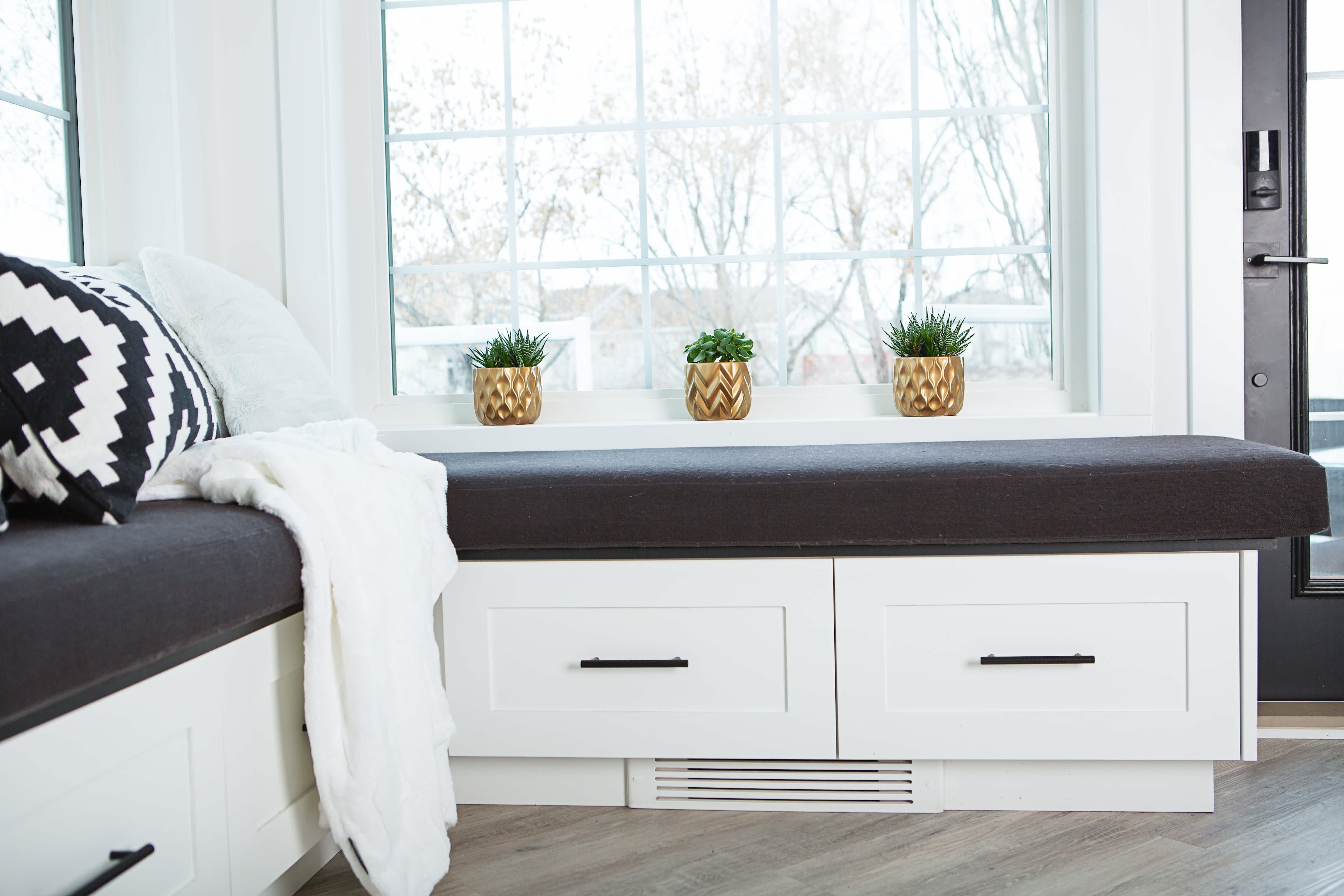 White built-in bench seating with dark gray cushions underneath large windows