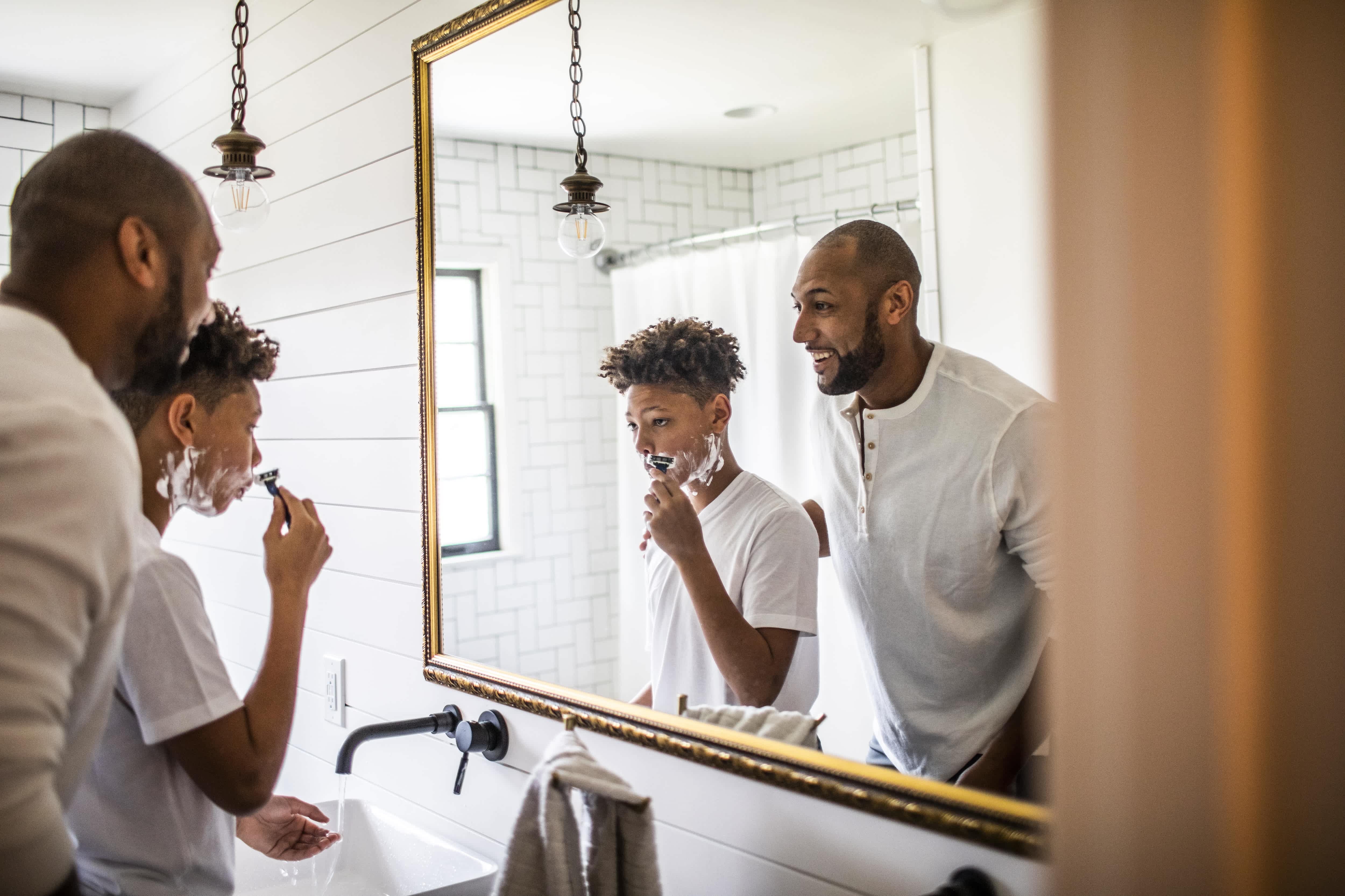 Father and son shaving in front of bathroom mirror