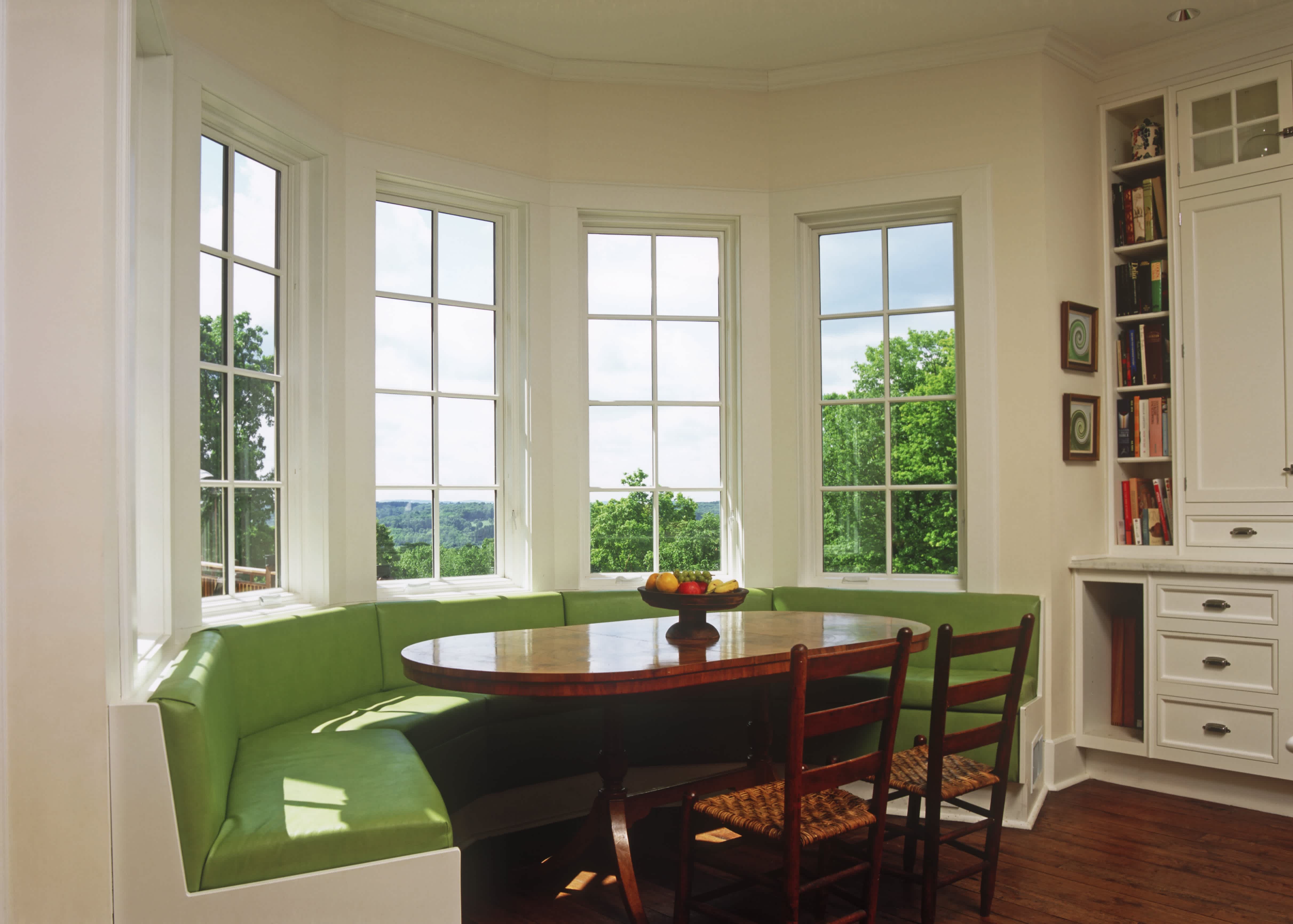A large, bright breakfast nook with an oval table and green upholstered seating