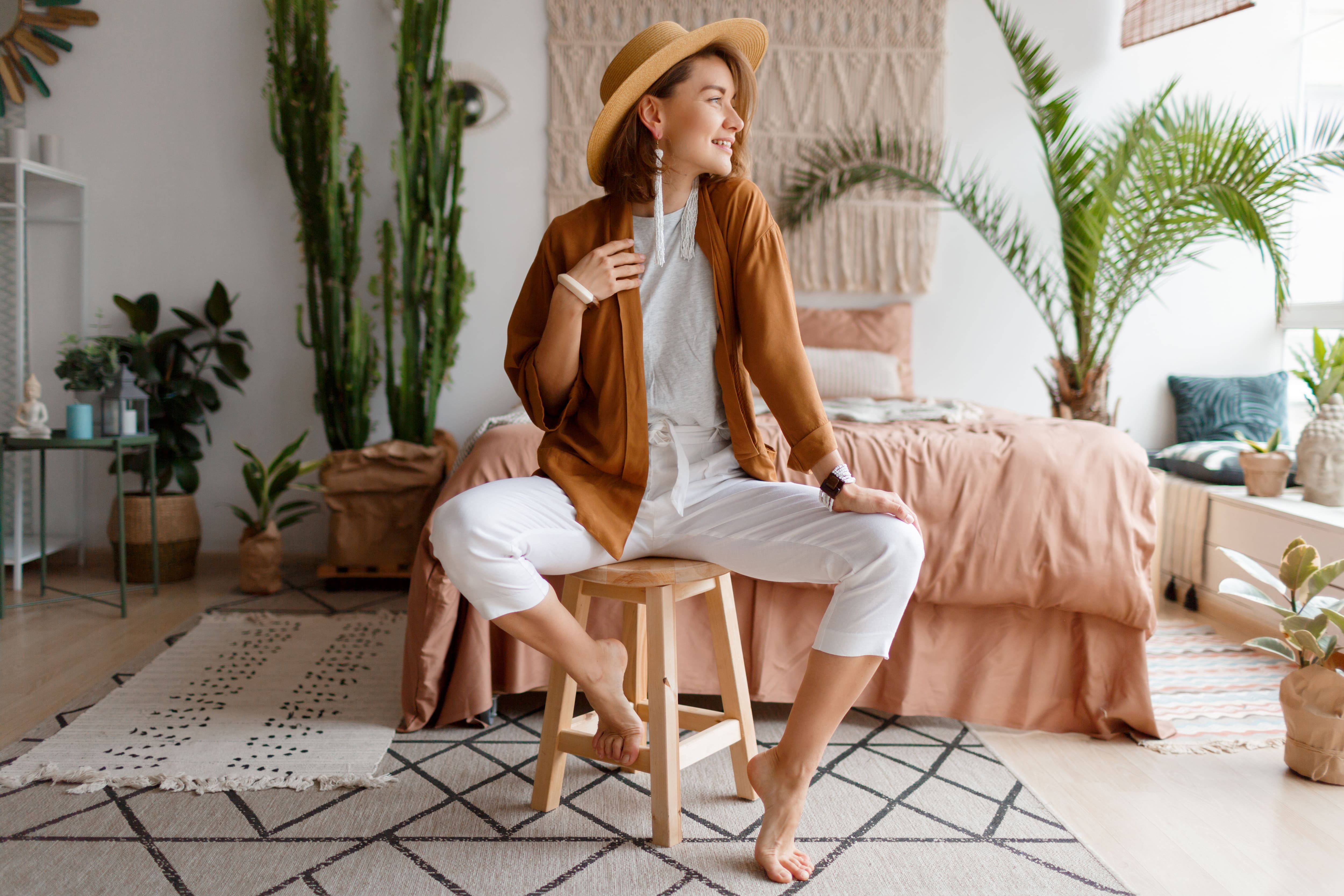 A fashionable young woman sitting on a wooden stool in front of her bed with a macrame headboard