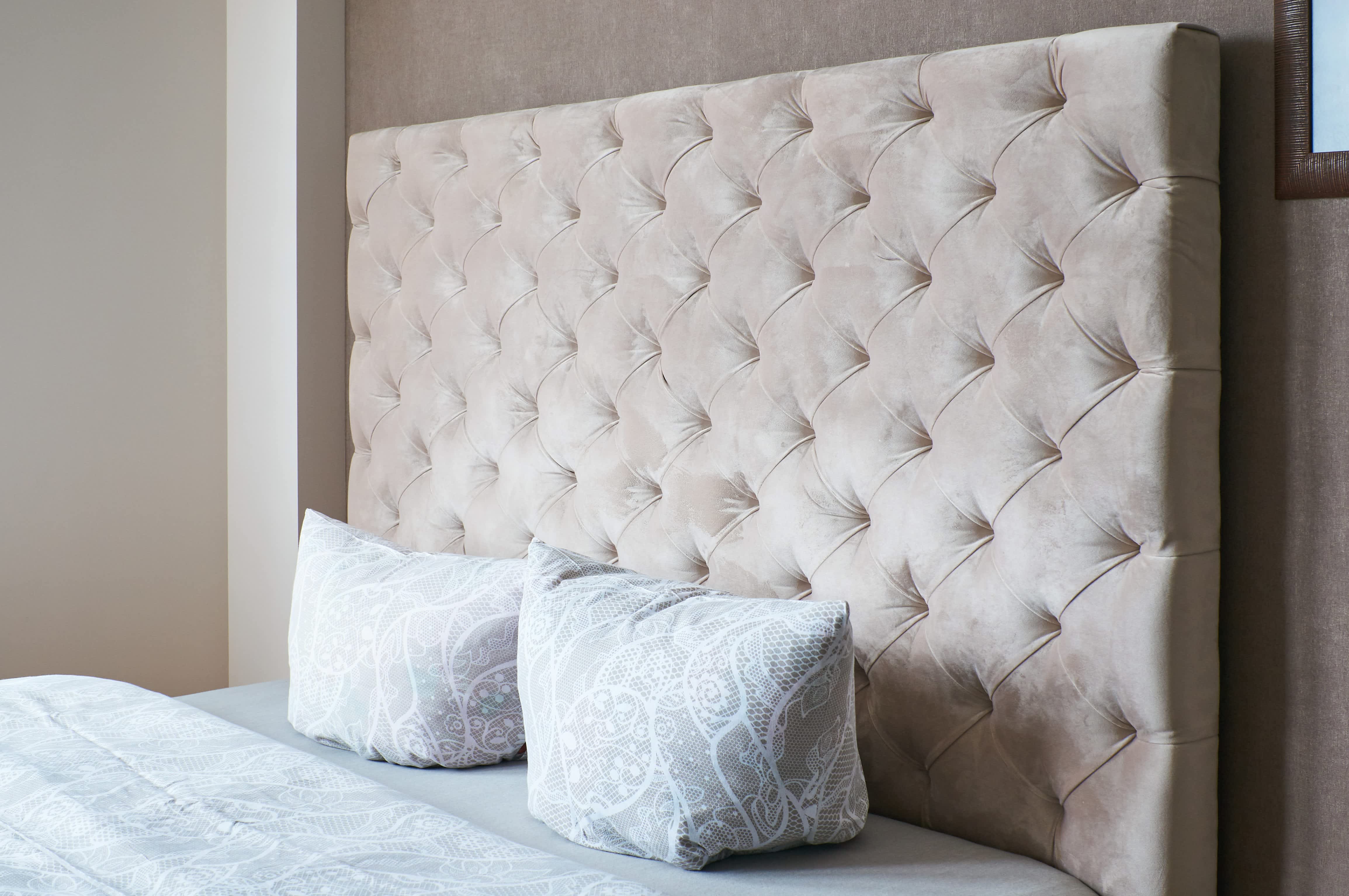 A simple bedroom with a tall, velvet, diamond tufted headboard