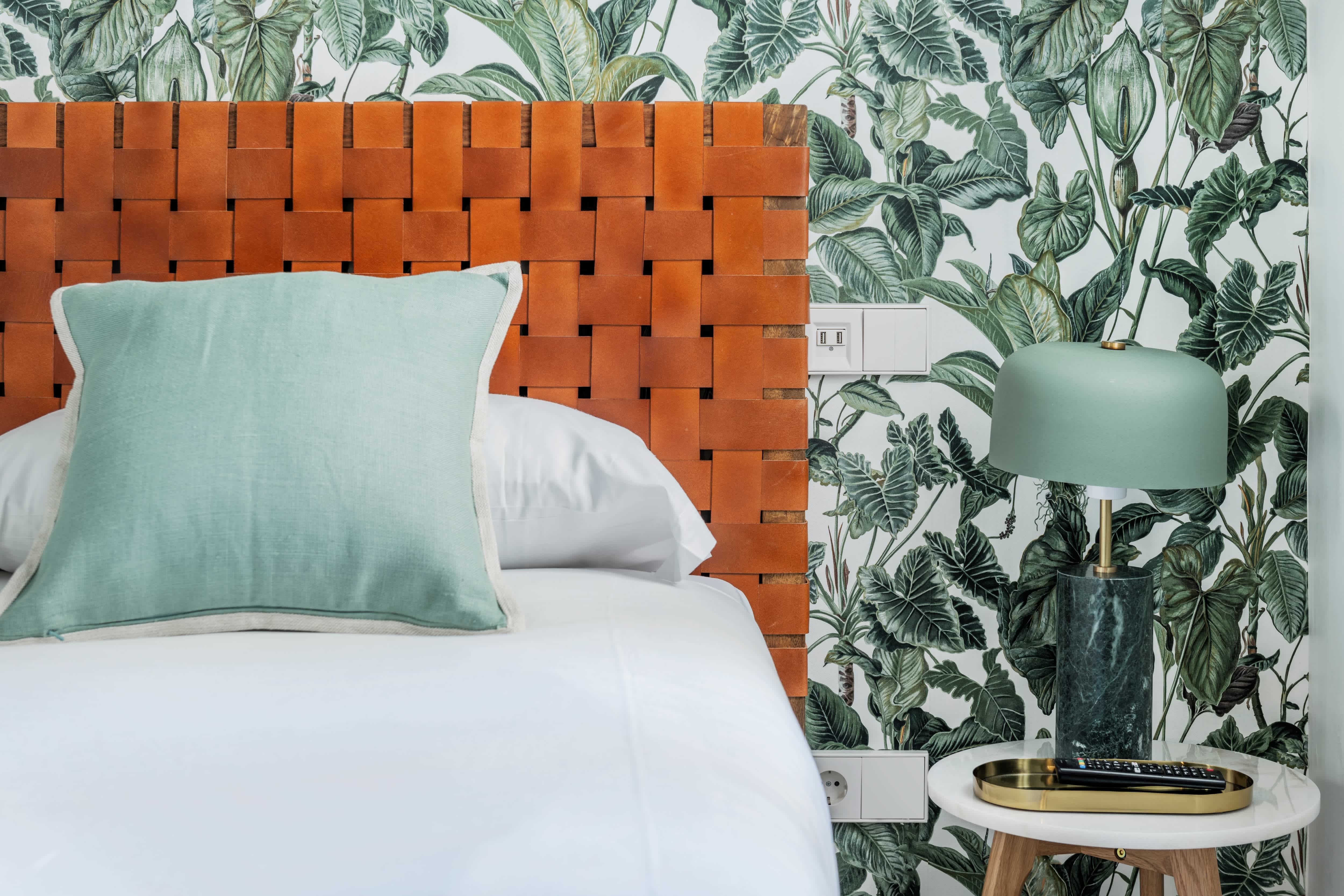 An eclectic green bedroom with plant wallpaper and a woven leather headboard