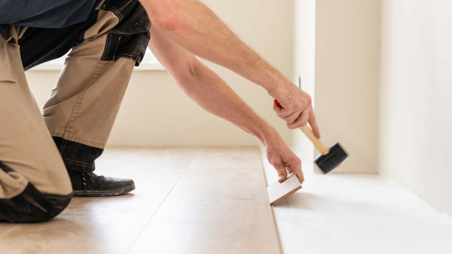 Professional installing laminate flooring using a soft hammer