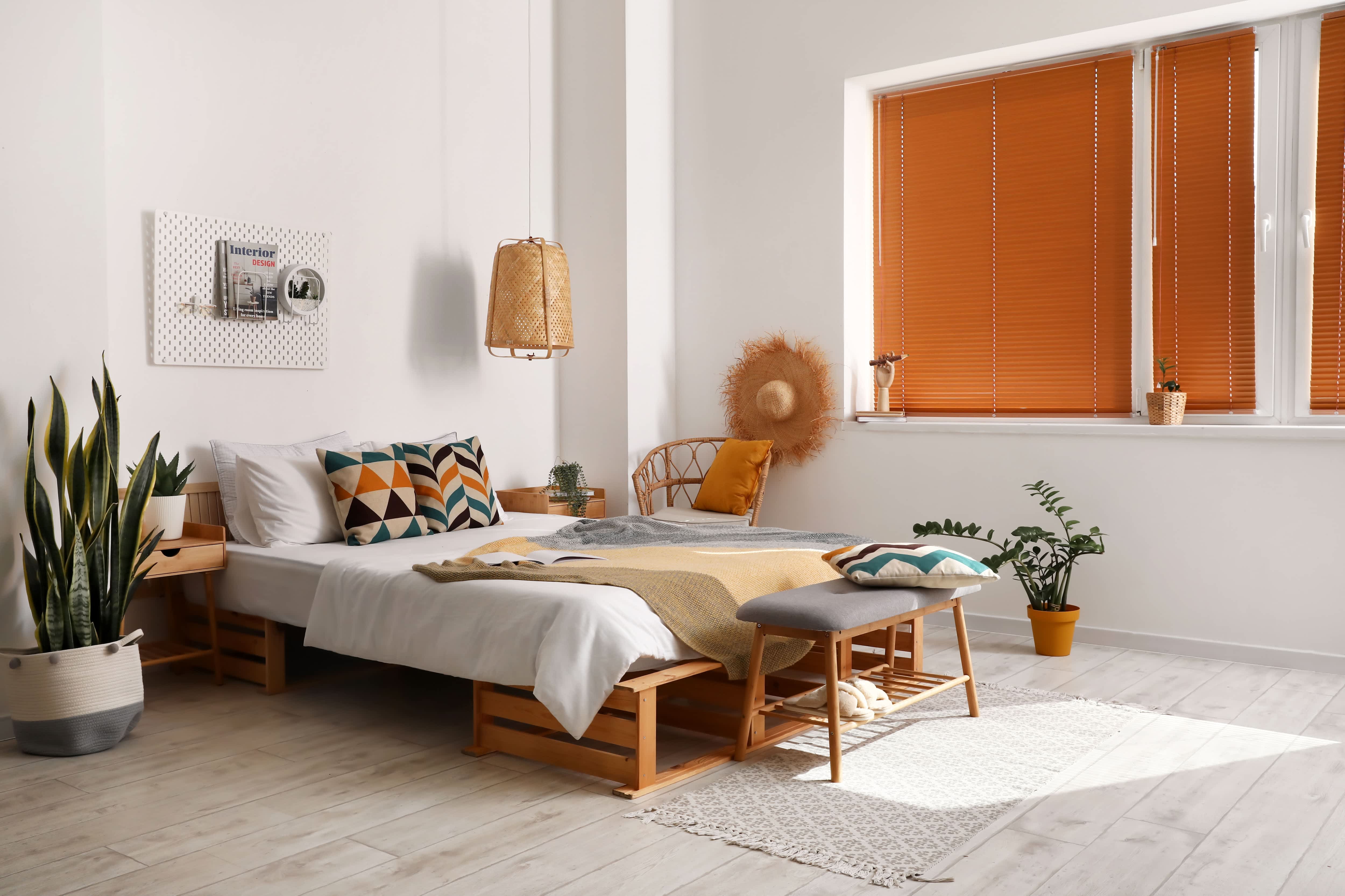 A modern bedroom with orange accents and a pegboard on the wall used as a headboard